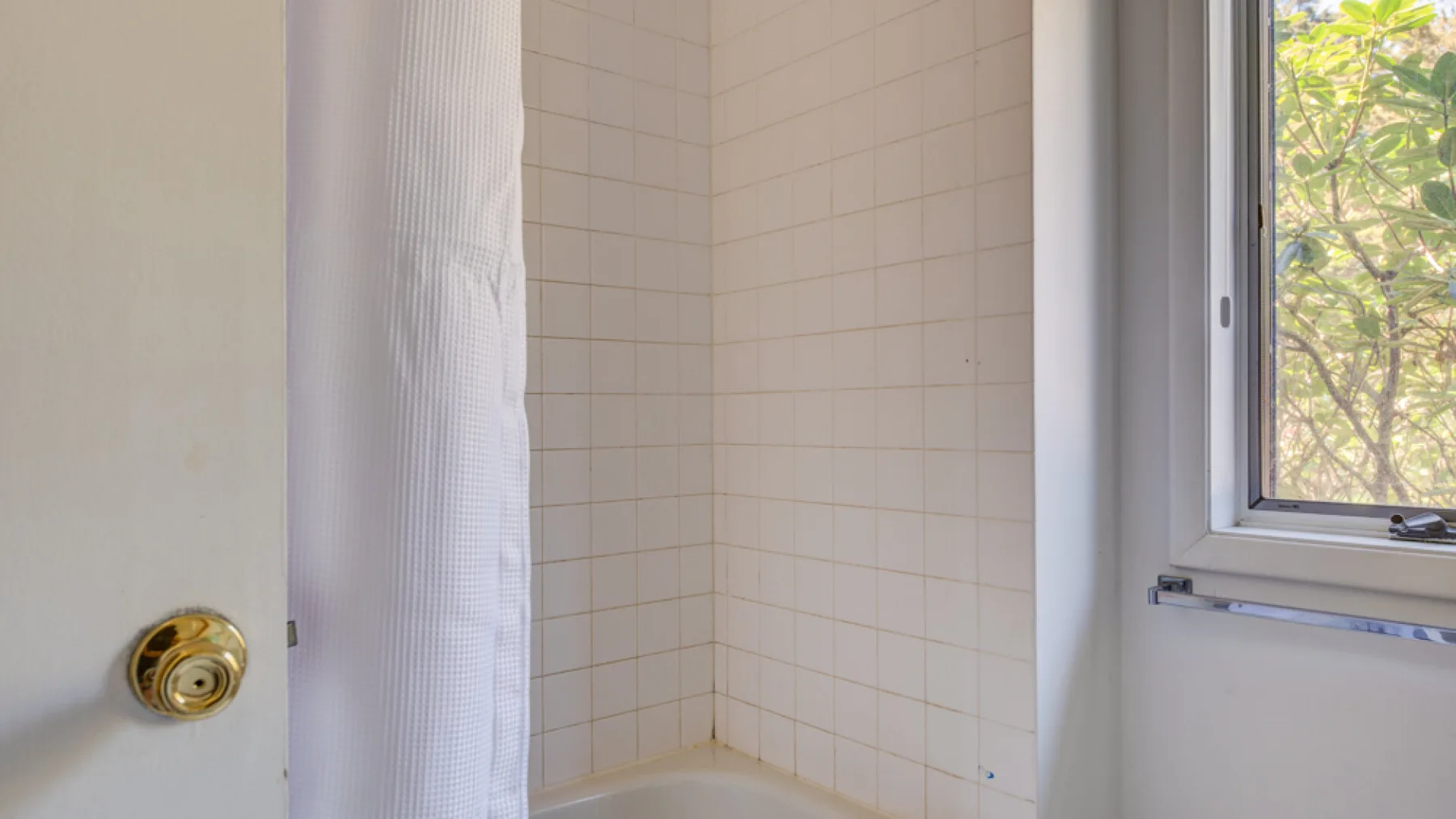 A tiled shower area with a curtain and a window.