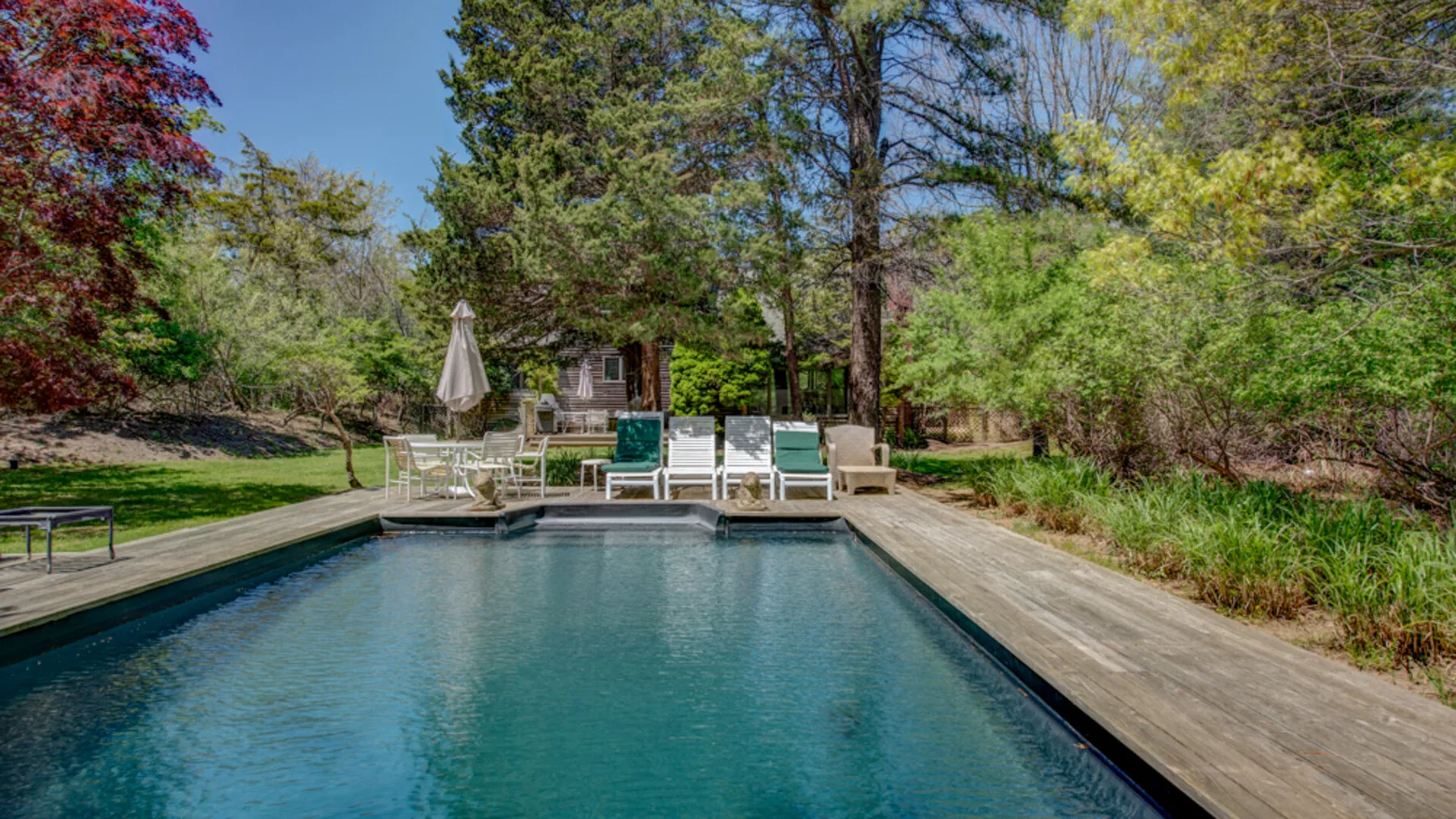 Una piscina al aire libre está bordeada por una terraza de madera y rodeada de árboles.