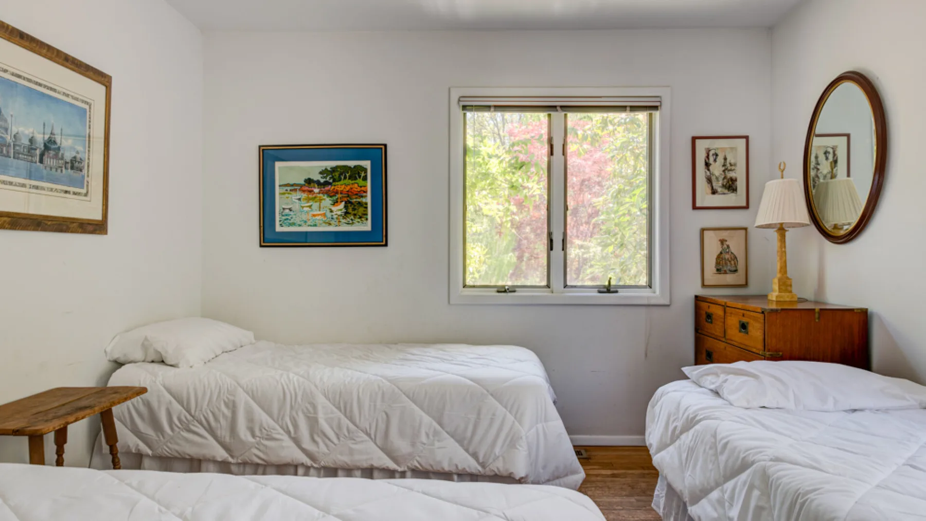A bright bedroom with two beds, framed artwork, and a window.