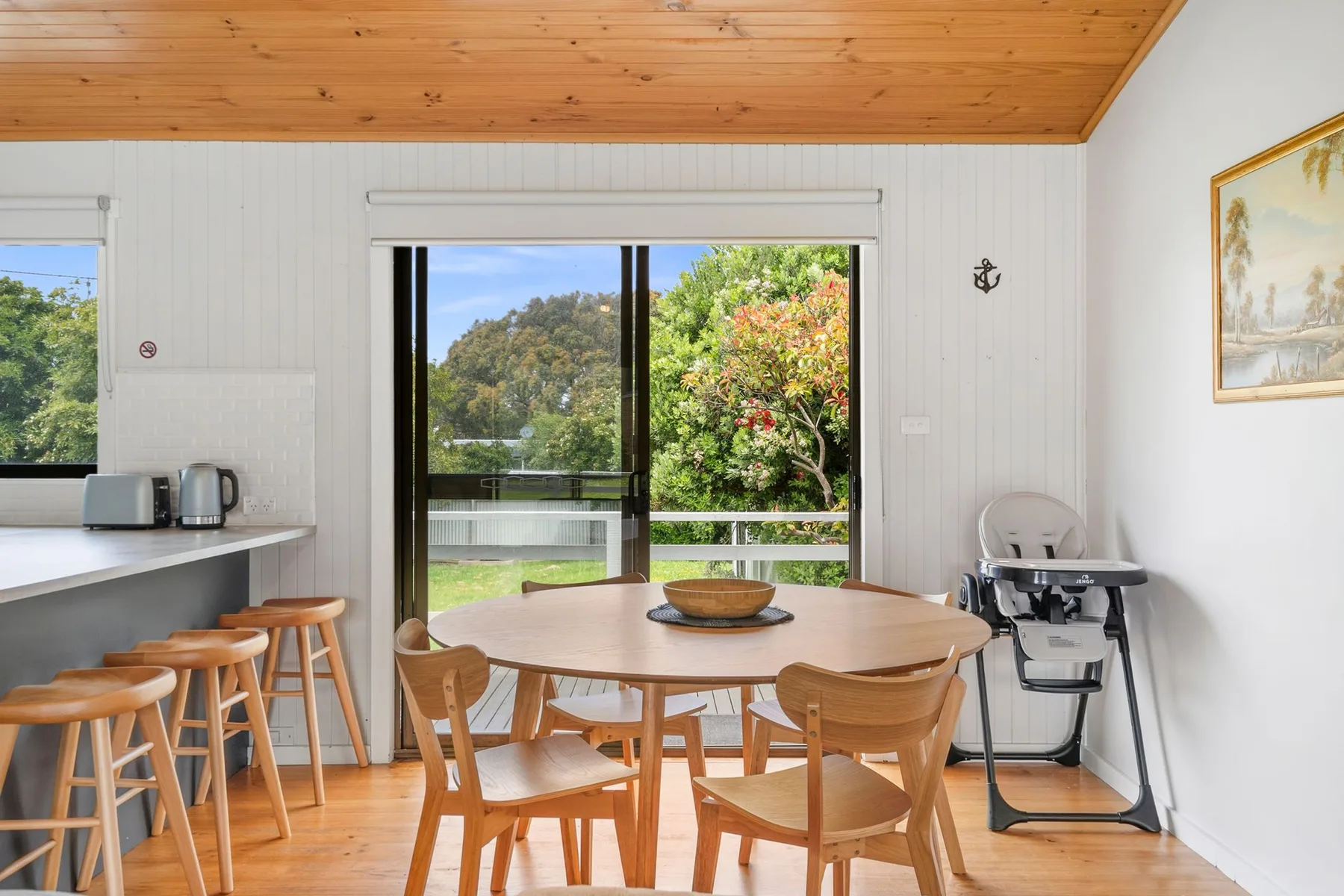A dining area with a round table beside sliding glass doors opening to greenery.