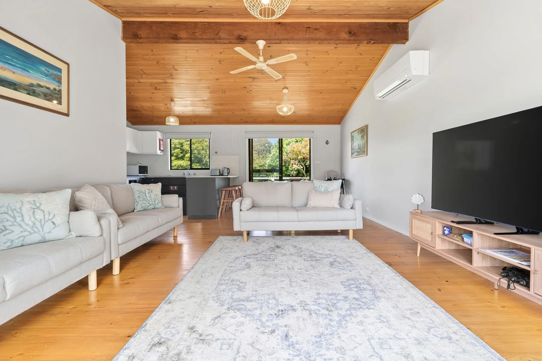 A bright living room with seating, a television, and an open kitchen.