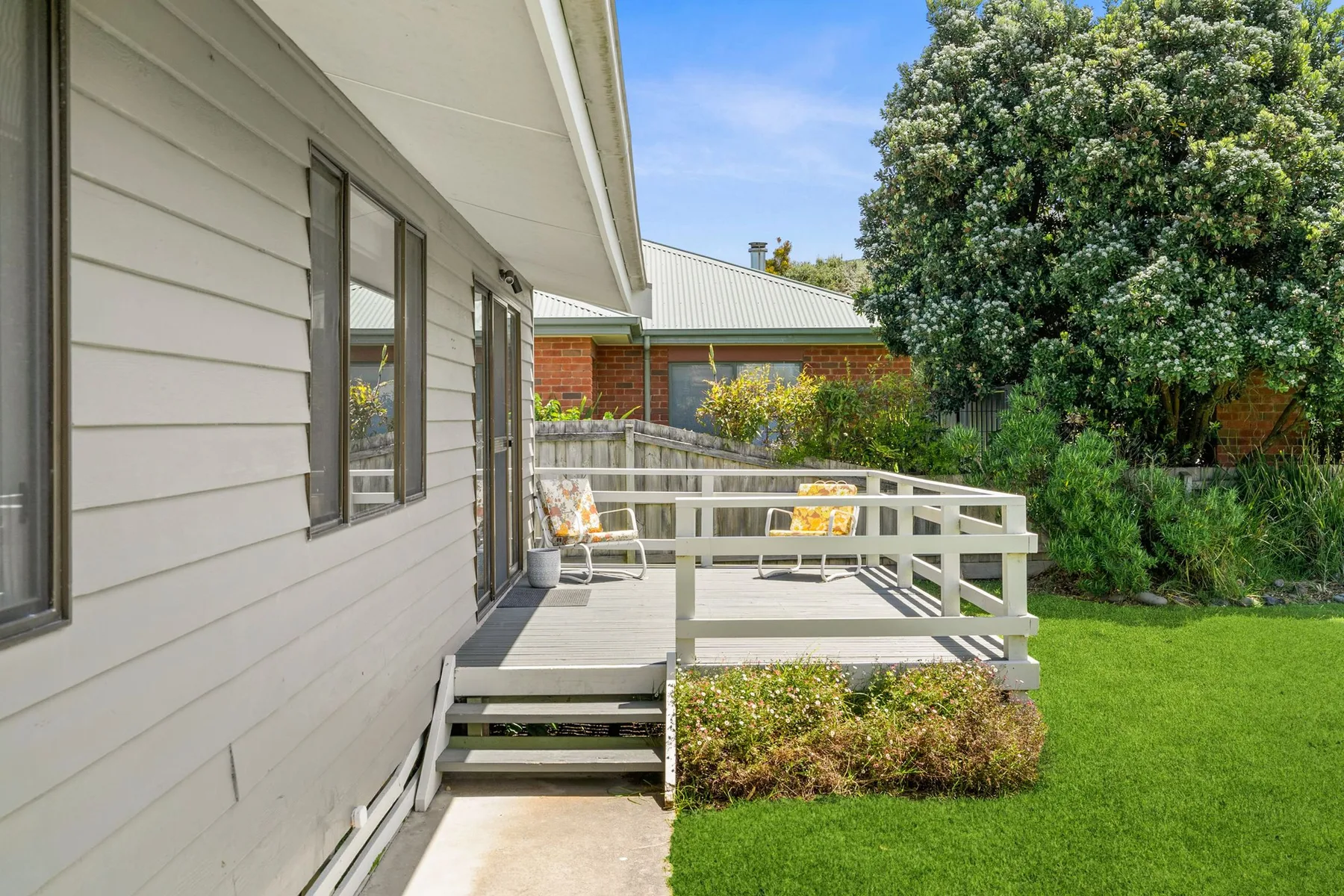 A house patio with white railings and a green lawn beside it.
