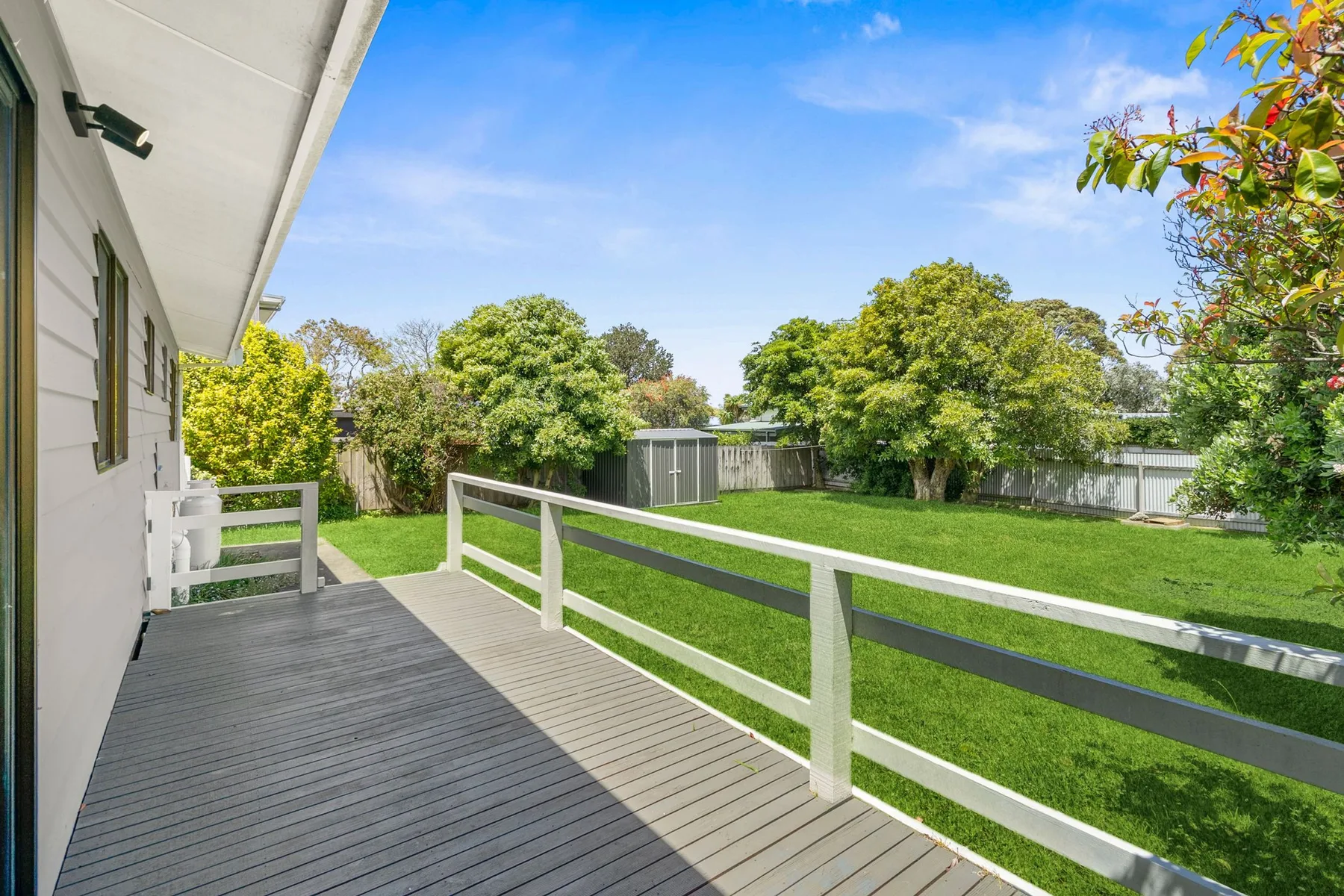 A raised deck overlooks a green yard bordered by trees and fencing.
