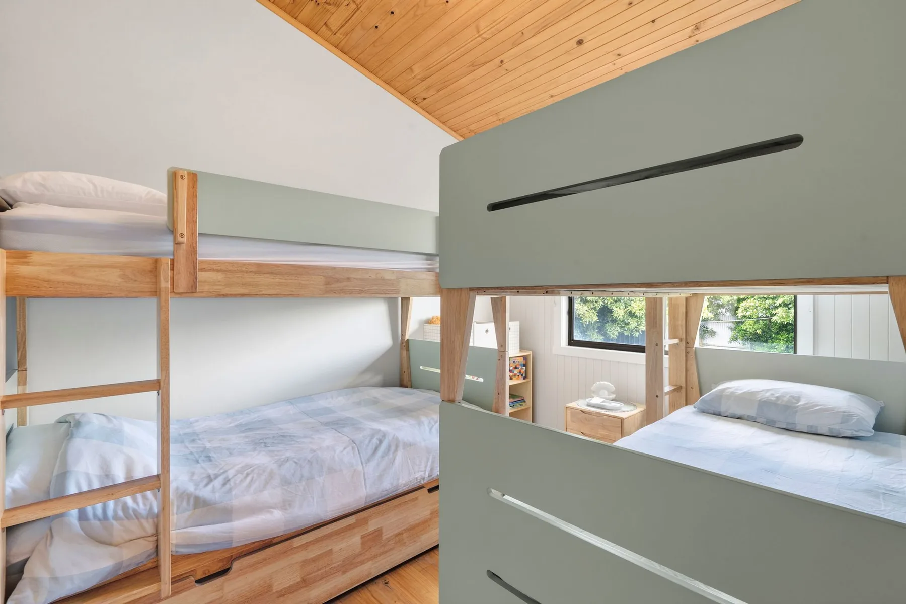 A bedroom with wooden bunk beds and a sloped wood ceiling.