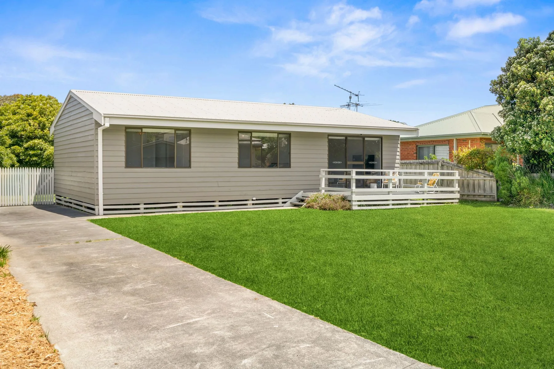 A single-story house with a small deck faces a green lawn.