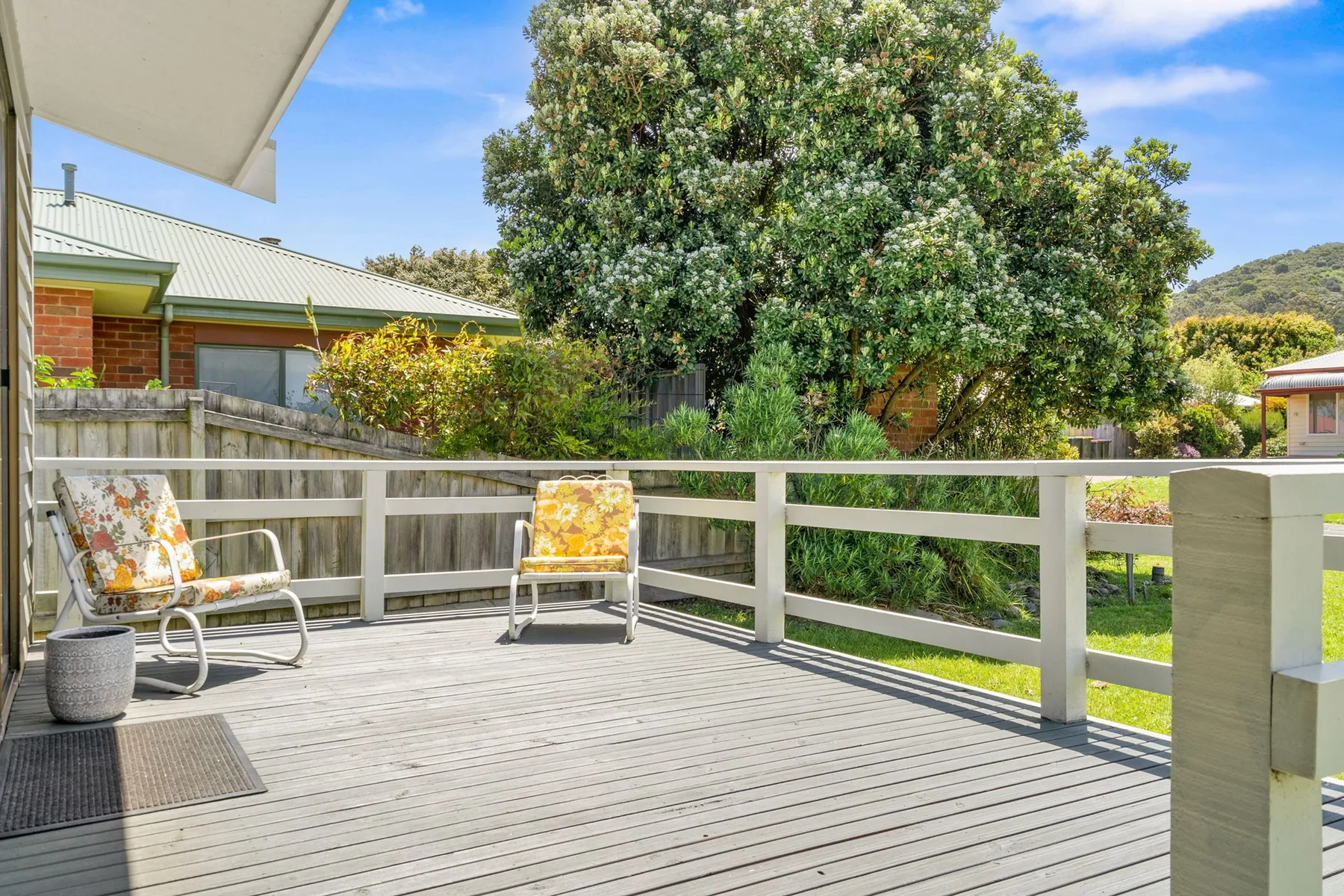 An outdoor deck with seating overlooks a leafy yard.