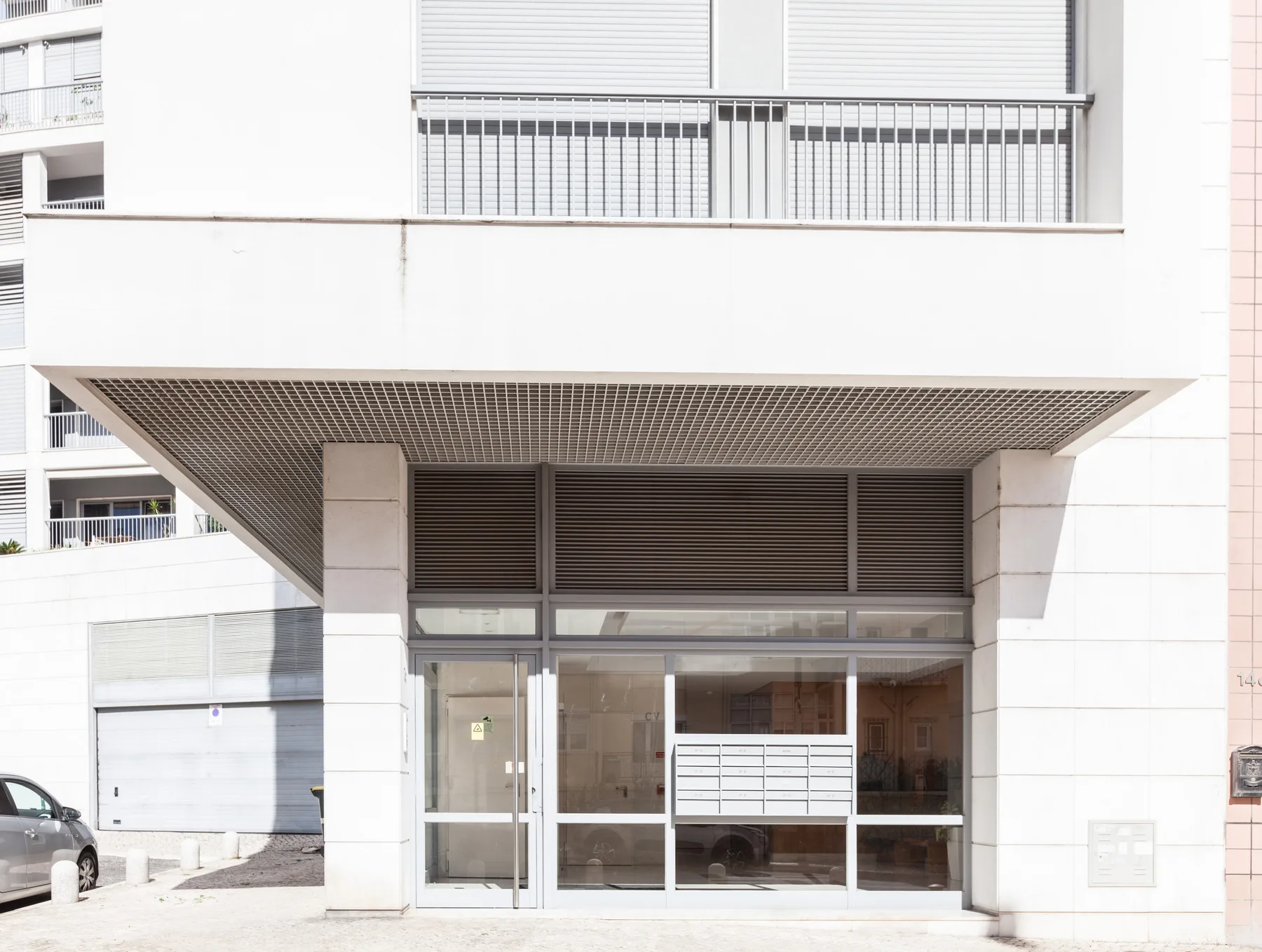 La entrada exterior de un edificio de apartamentos moderno, con puertas de vidrio y un balcón encima.