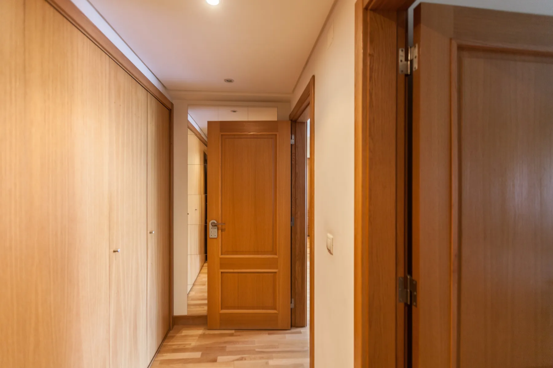 Un pasillo con puertas de madera y paredes claras.