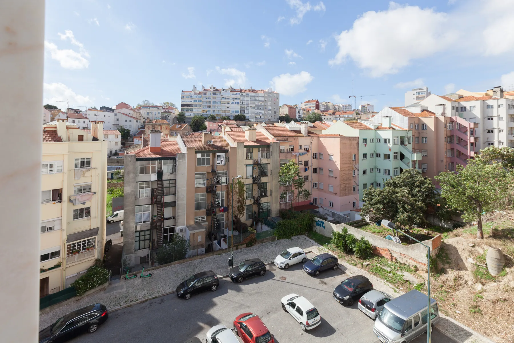 Vista urbana de edificios de apartamentos y coches aparcados bajo un cielo parcialmente nublado.