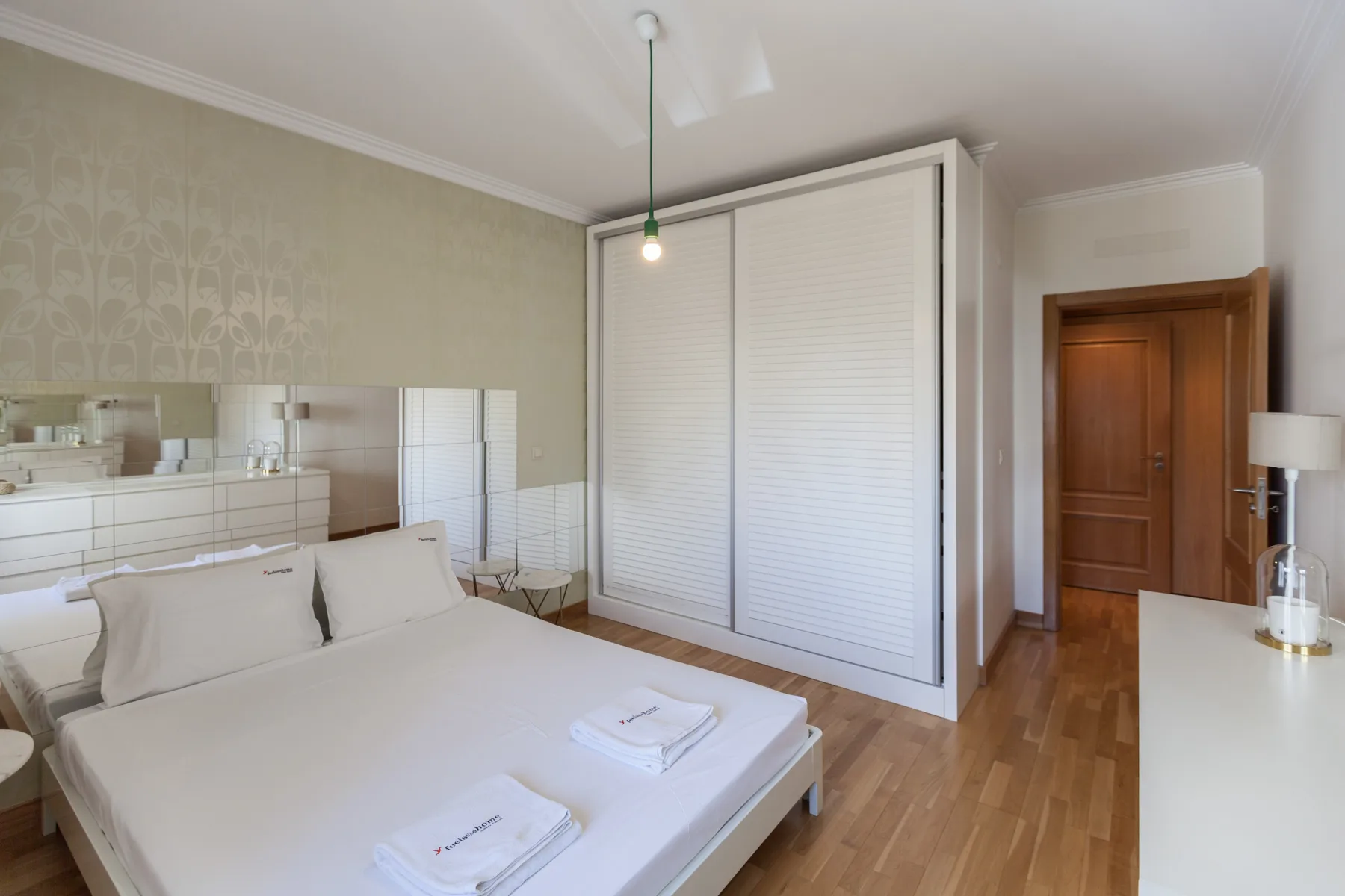 Un dormitorio con una cama, paneles de espejo y un armario blanco.