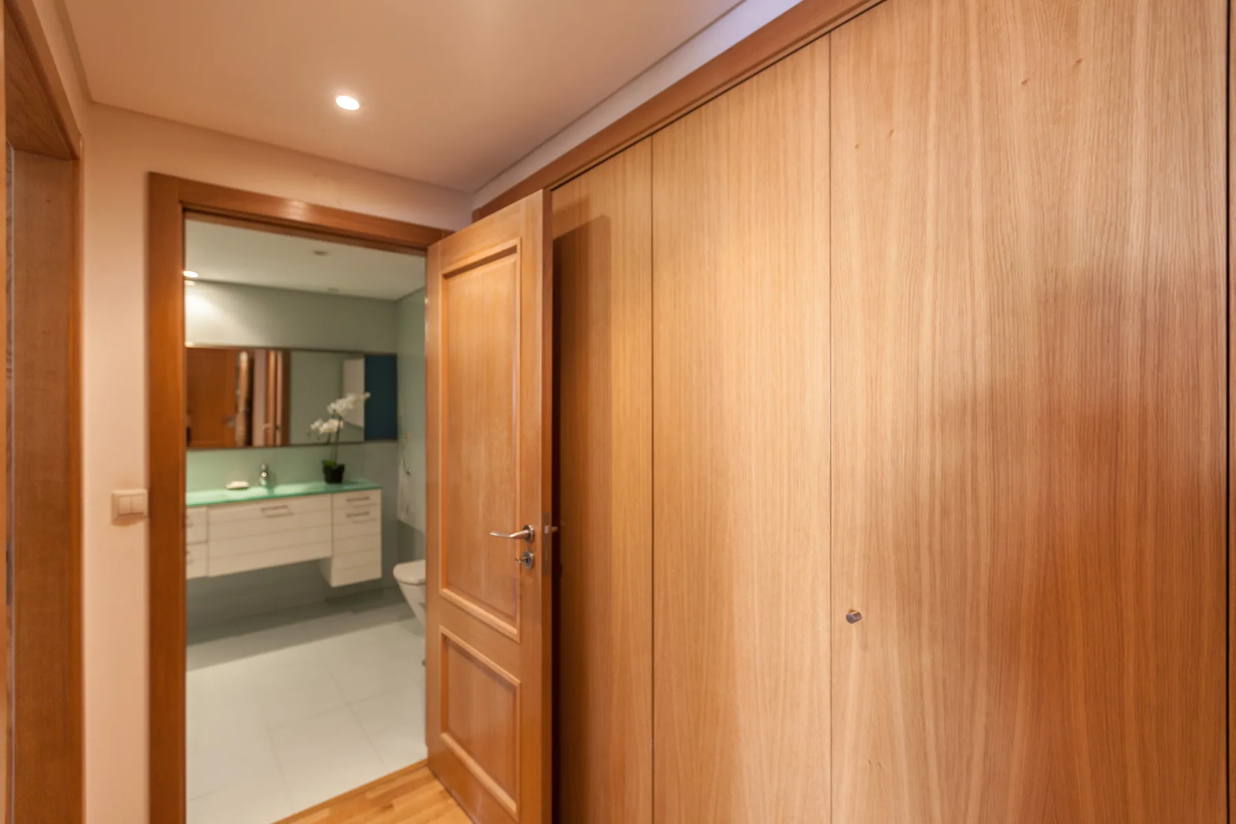 Un pasillo con puertas de madera da a un baño con lavabo.