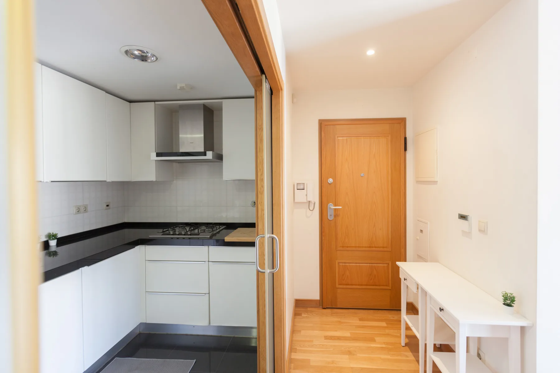 Un recibidor estrecho se abre junto a una cocina compacta con armarios blancos.