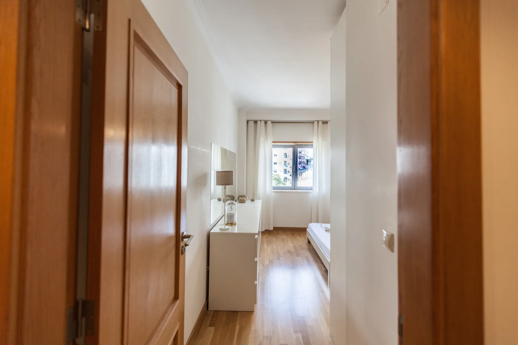 Un dormitorio con una cama, una mesita y una ventana al fondo.