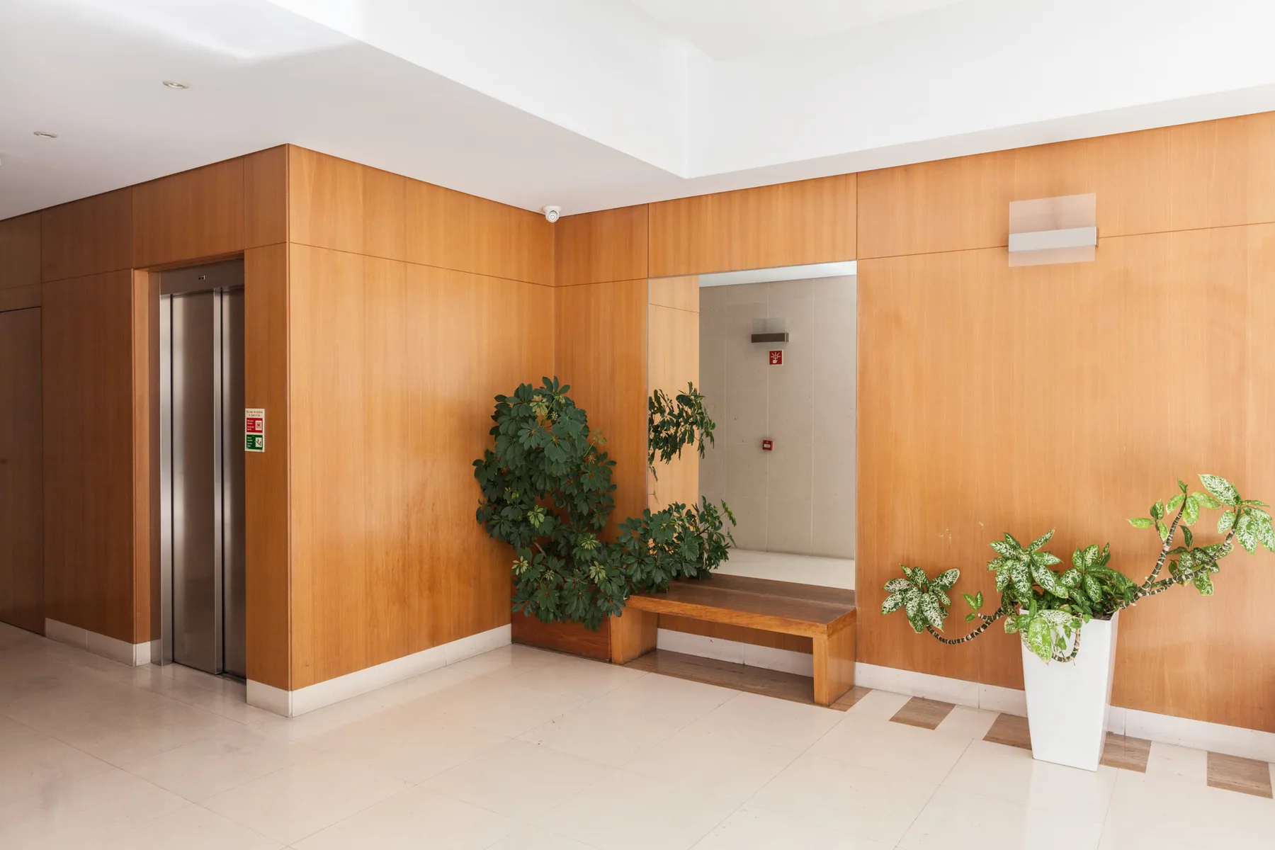 Un vestíbulo interior con ascensor, un banco y plantas en macetas.