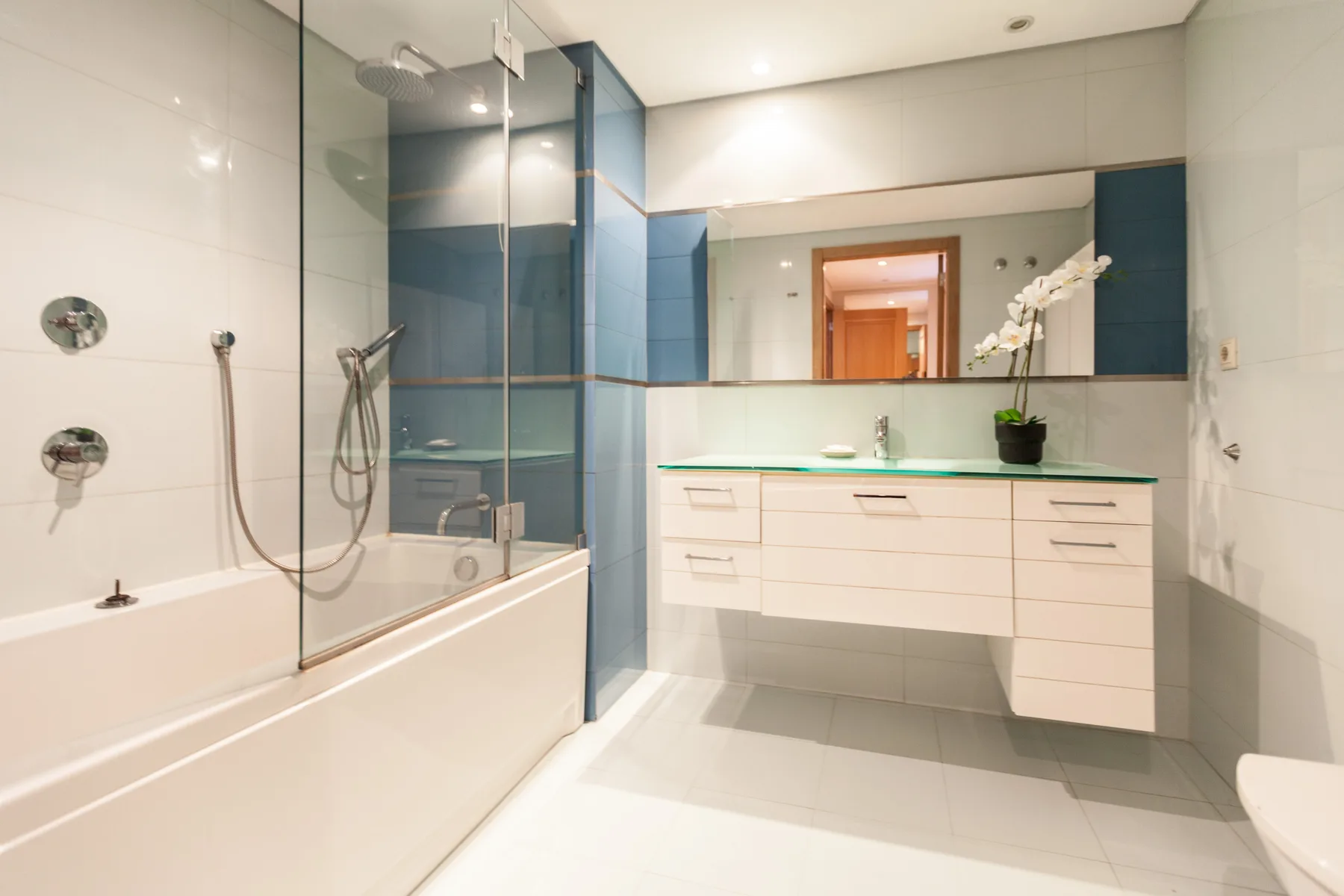 Un baño luminoso con bañera, mampara de ducha de vidrio y lavabo suspendido.