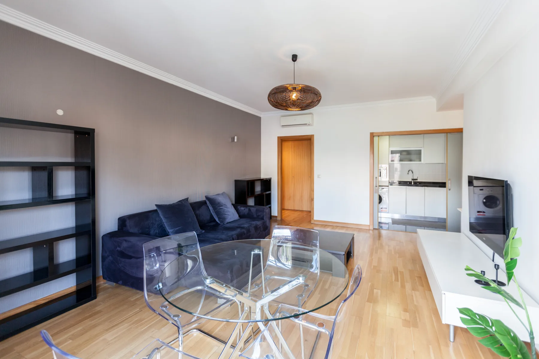 Una sala de estar y comedor con mesa de vidrio, asientos y cocina abierta.