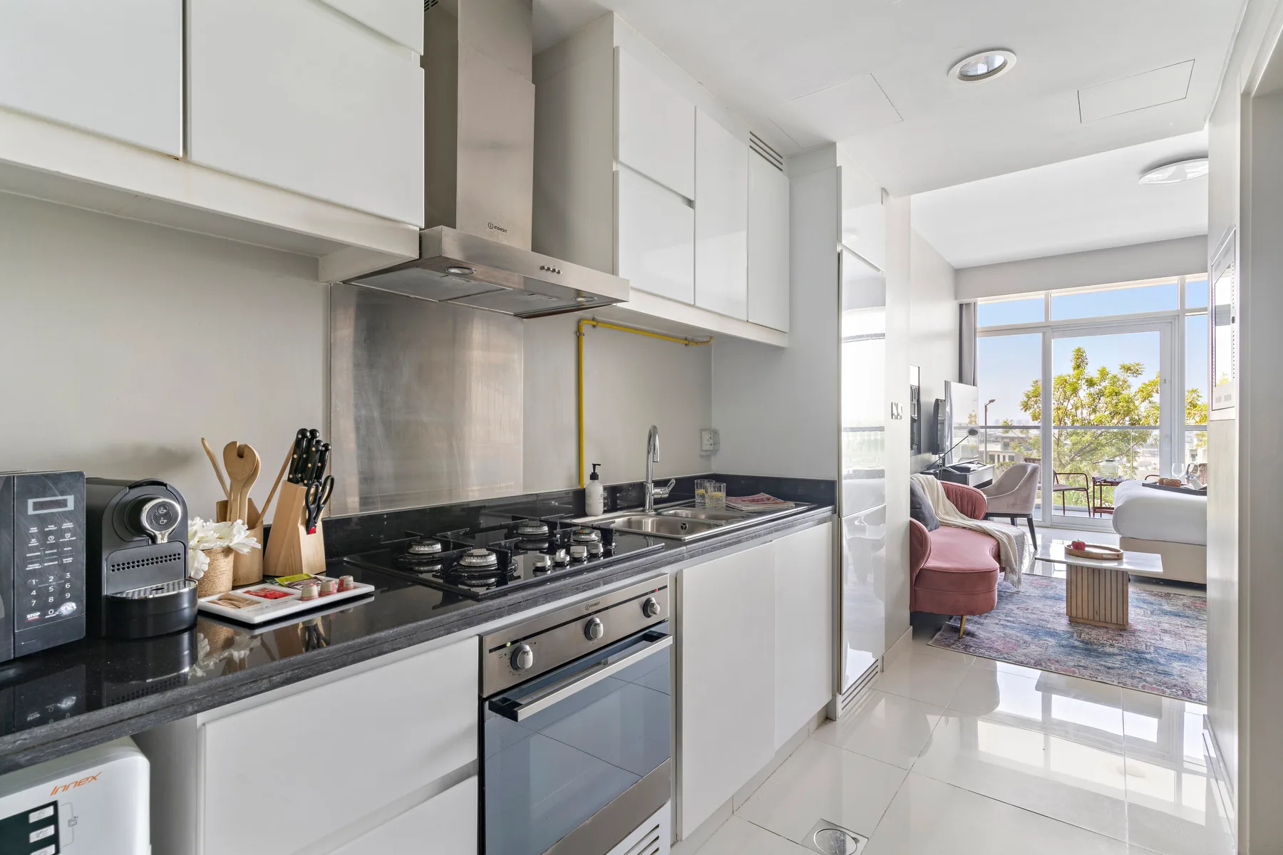 A modern kitchen with dark countertops opens onto a bright living area.