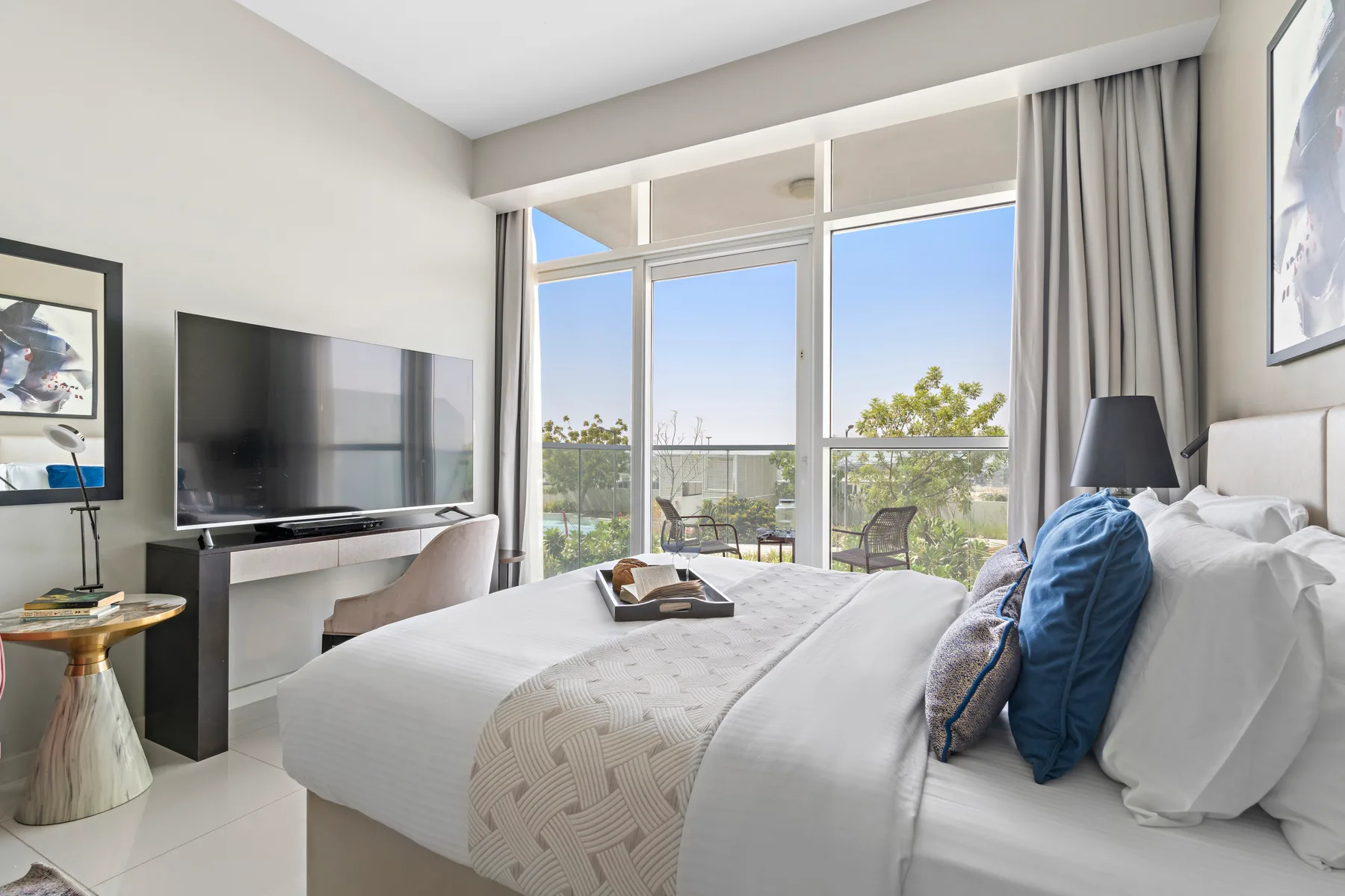 A bright bedroom with a large bed beside floor-to-ceiling windows.