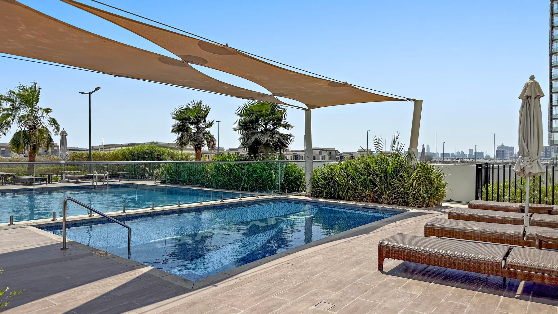 An outdoor pool sits beneath a fabric shade canopy, with lounge seating nearby.