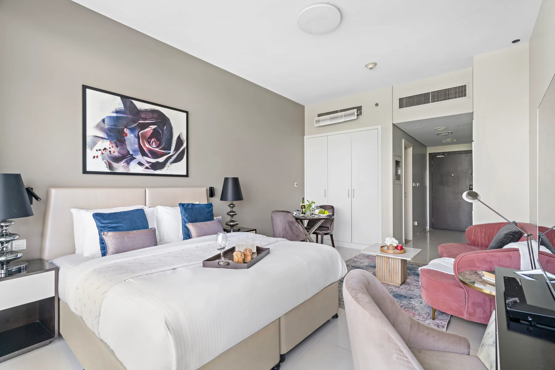 A bedroom with a large bed, abstract wall art, and a small seating area.