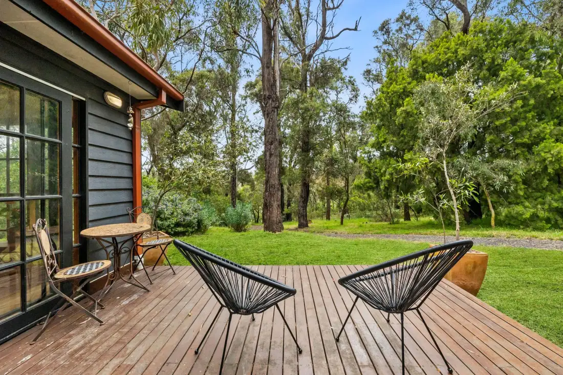 Una terraza de madera con asientos al aire libre da a un césped verde y árboles.