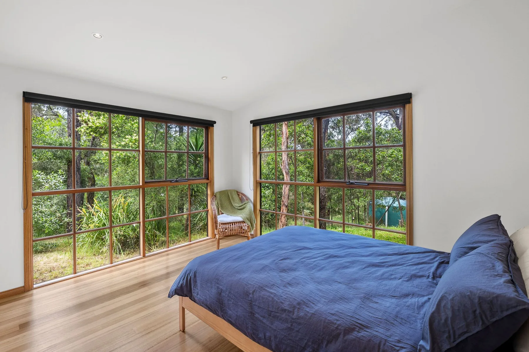 Un dormitorio con una cama y grandes ventanales que dan a zonas verdes.