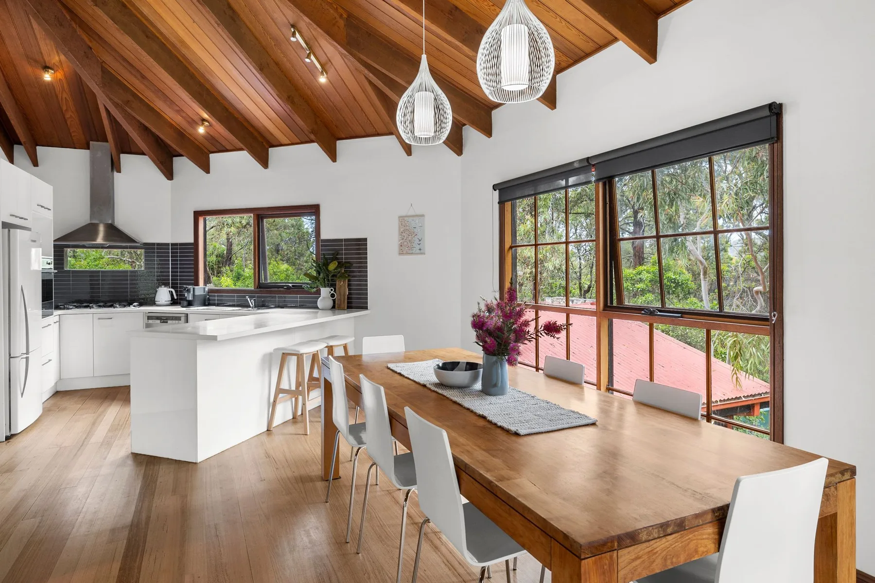 Una cocina abierta y zona de comedor con grandes ventanas con vistas a los árboles.