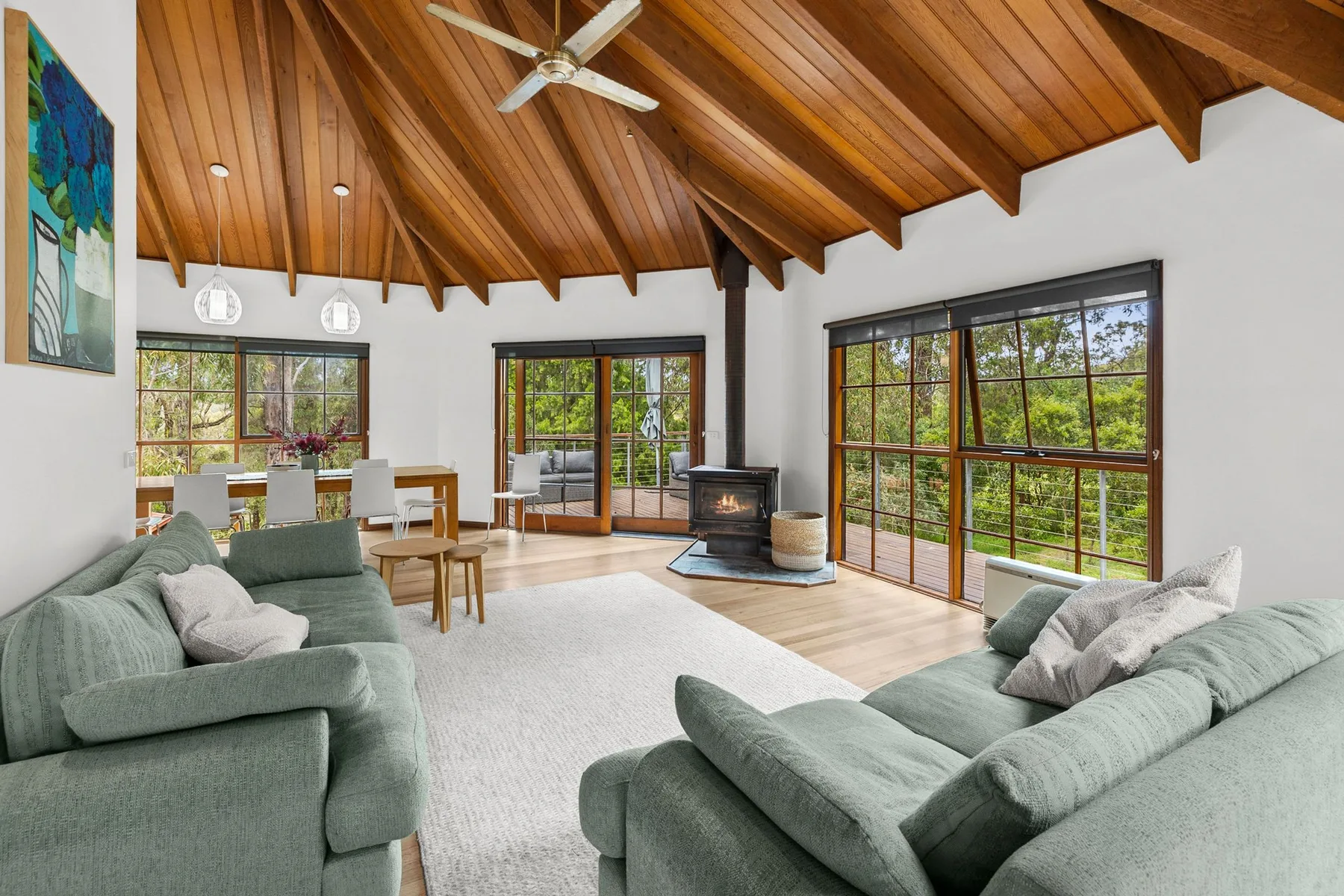Una sala de estar luminosa con asientos verdes, grandes ventanas y techo de madera.