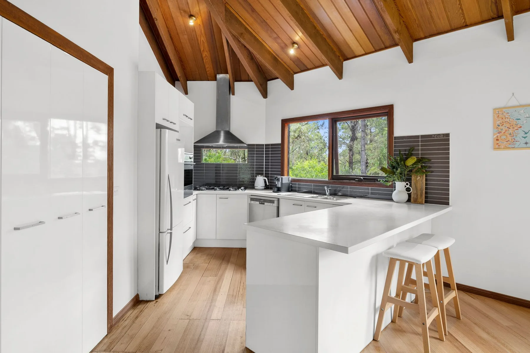 Una cocina luminosa con muebles blancos, una isla central y un techo revestido de madera.