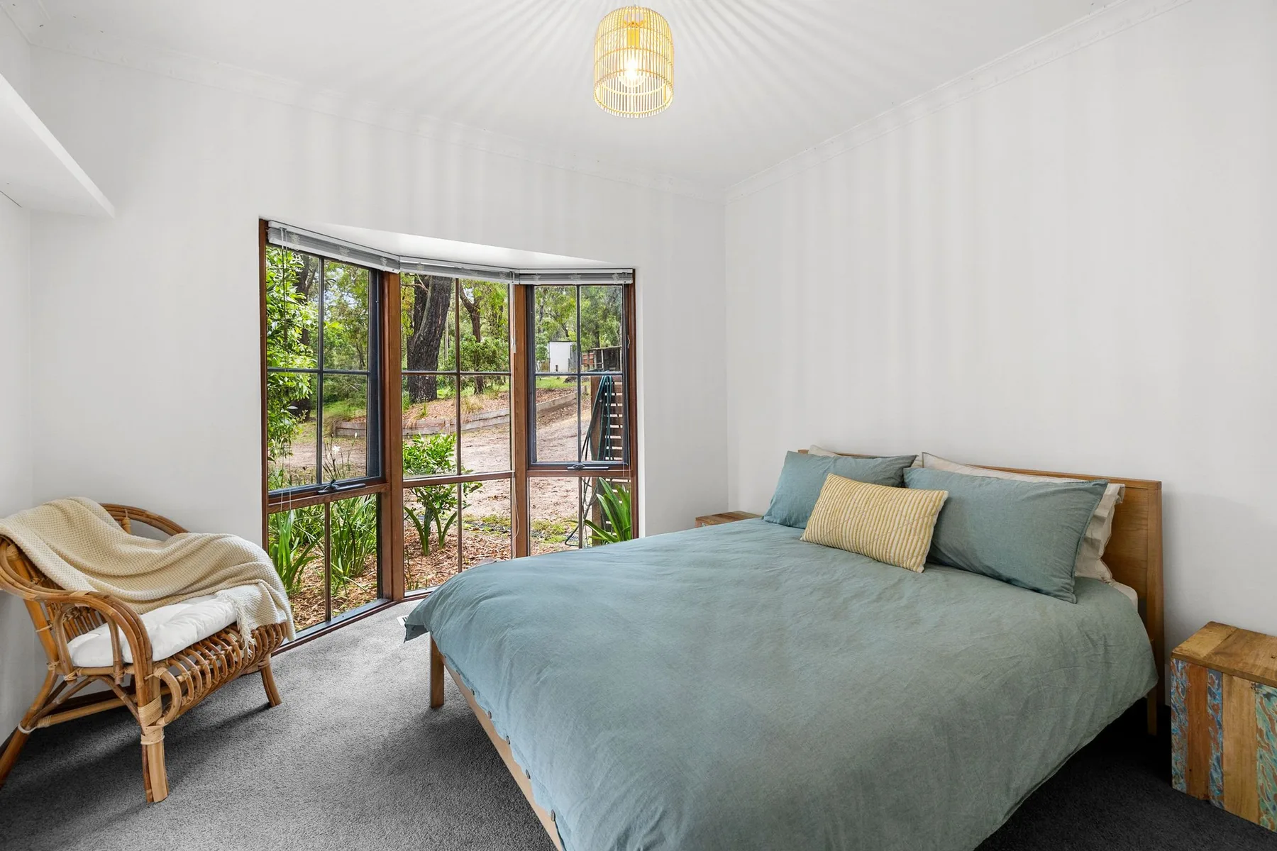 Un dormitorio con una cama grande y una ventana curva con vistas a la vegetación.