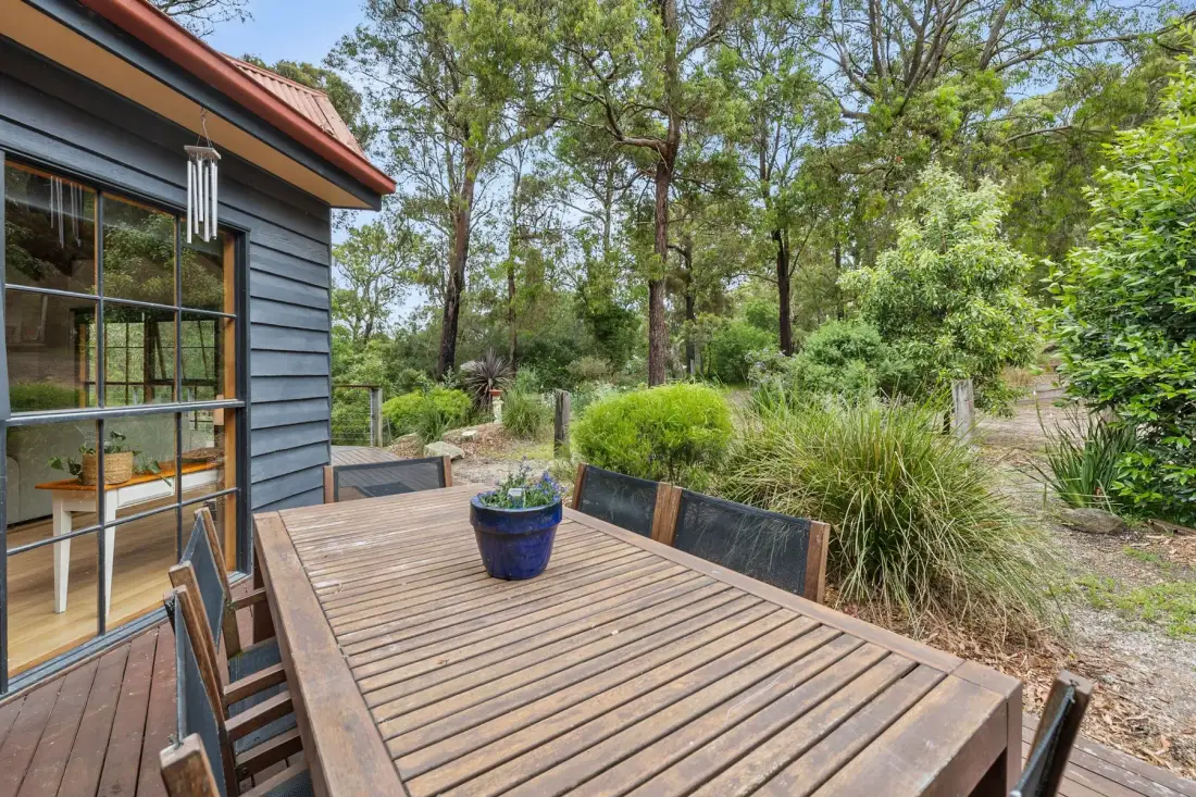 Una terraza exterior de madera con asientos da a un jardín rodeado de árboles y arbustos.