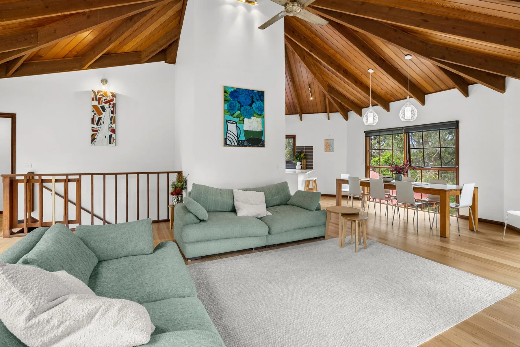 Una zona de estar y comedor con asientos verdes, techo de madera y grandes ventanas.