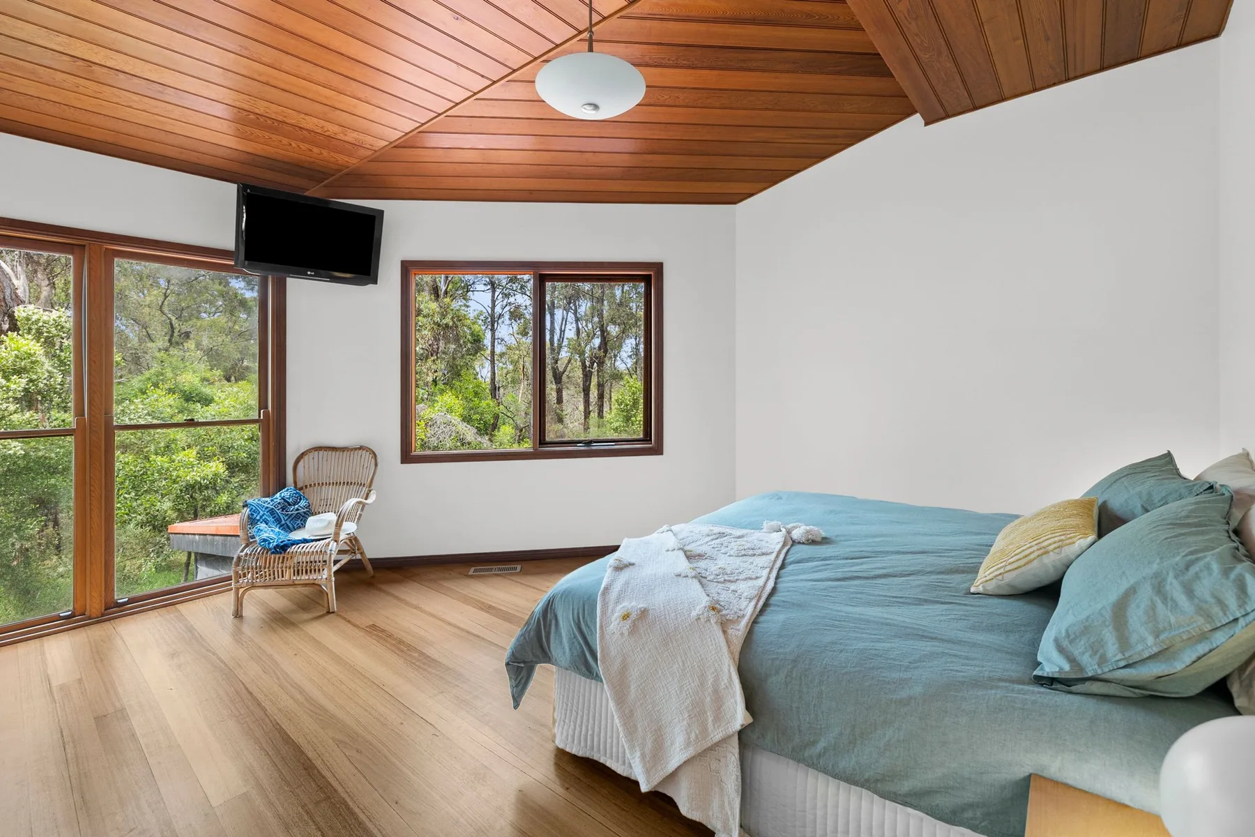 Un dormitorio con una cama, un techo de madera y ventanas con vistas a los árboles.
