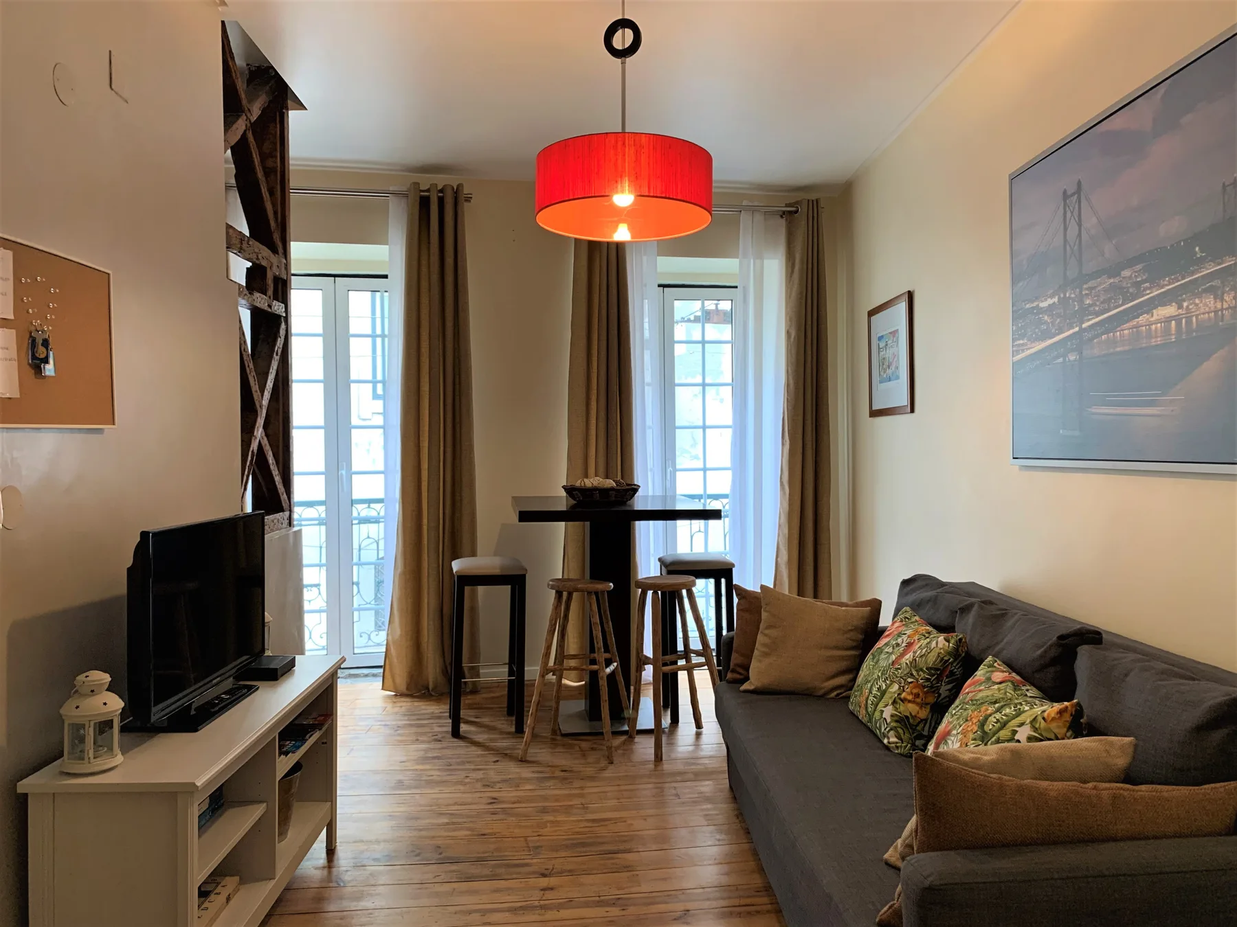 A living room with a sofa, television, and high table beside tall windows.