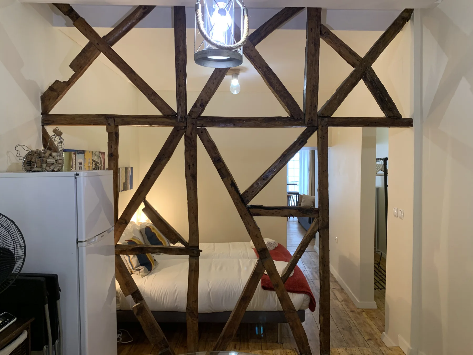 A bedroom with a bed behind dark exposed wooden beams.