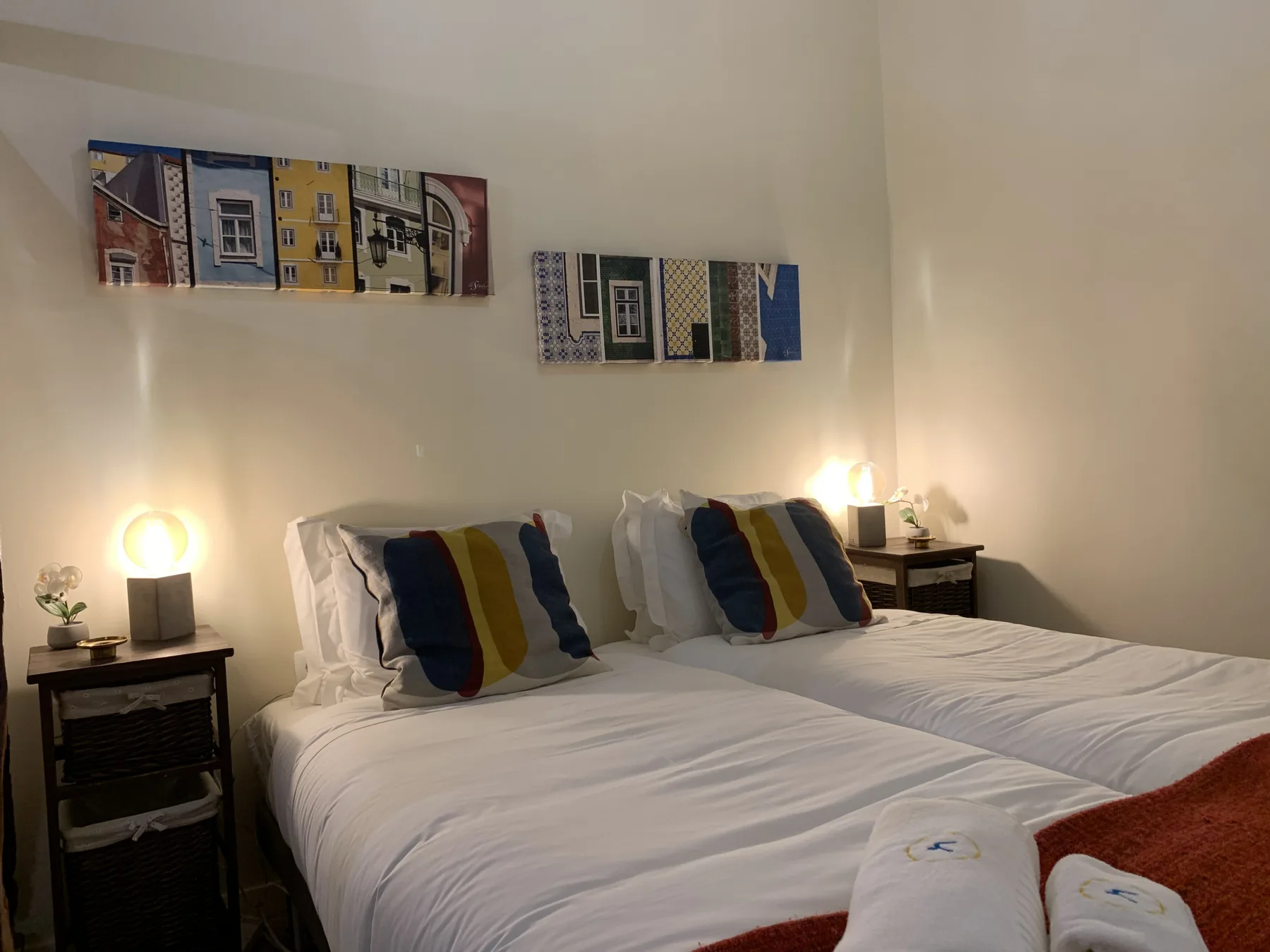 A bedroom with two beds, colorful pillows, and framed artwork on the wall.