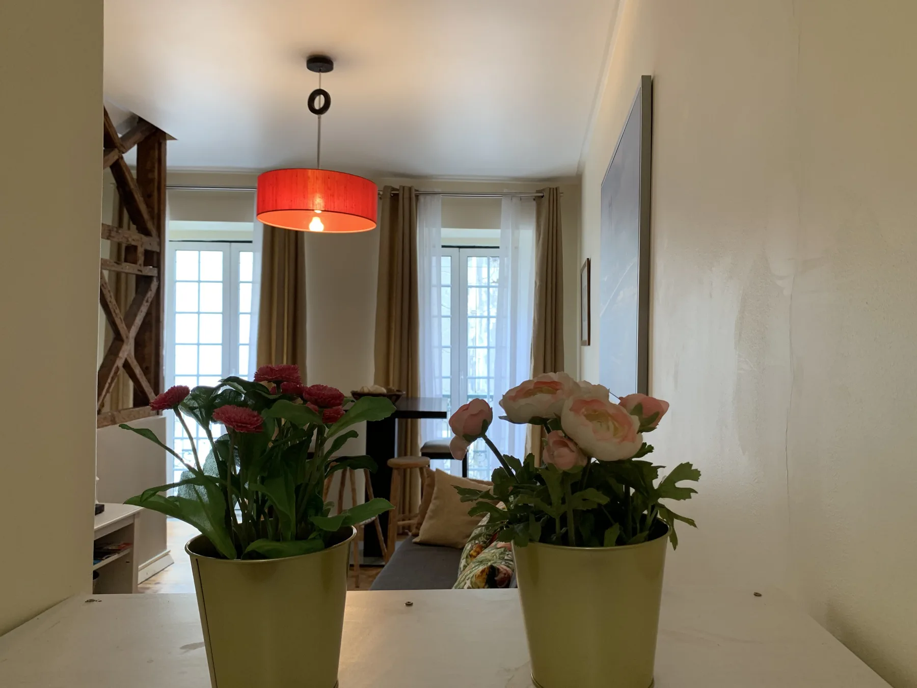 A bright living room with potted flowers on a counter and tall windows.