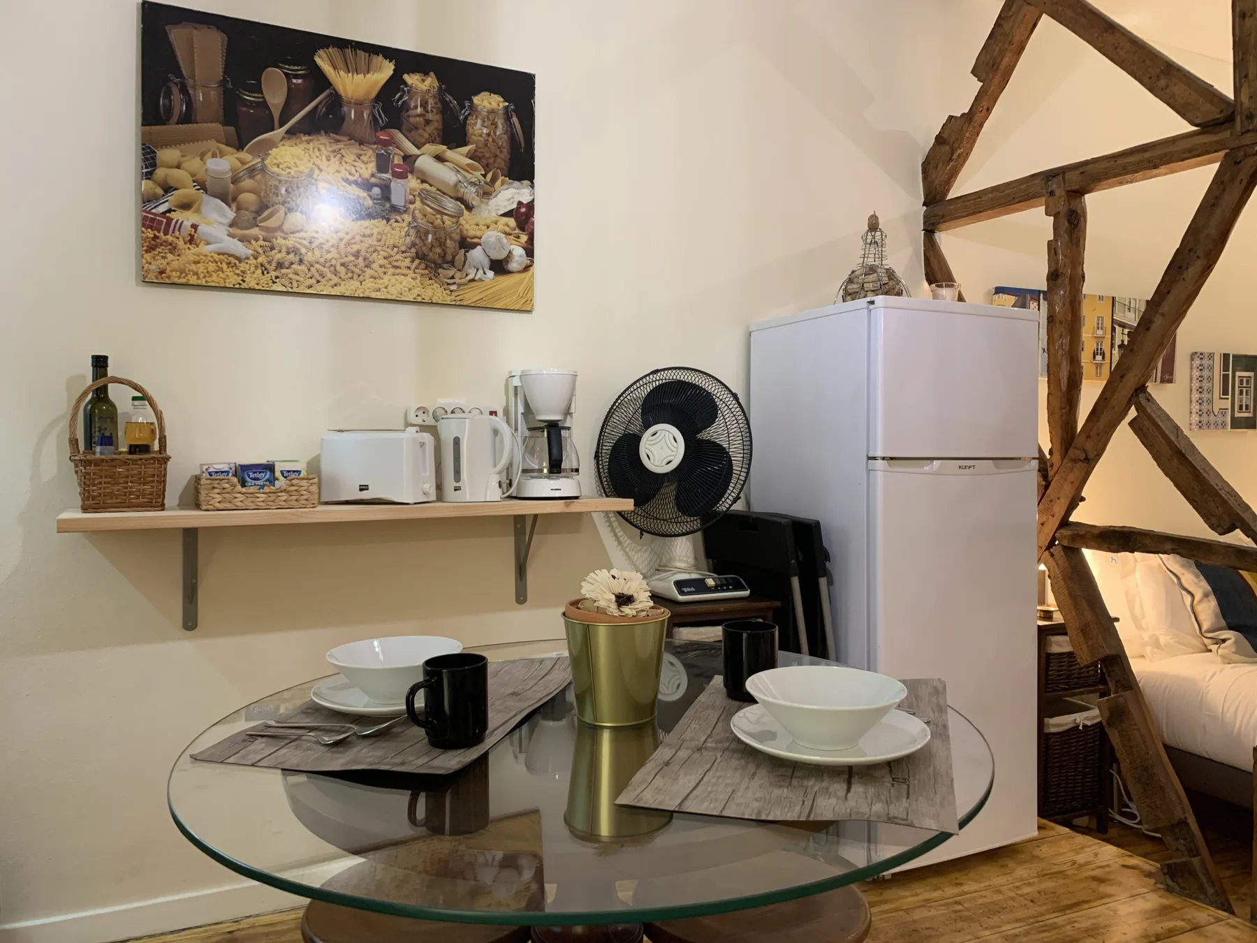 A compact dining and kitchen area has a glass table, small appliances, and a refrigerator.