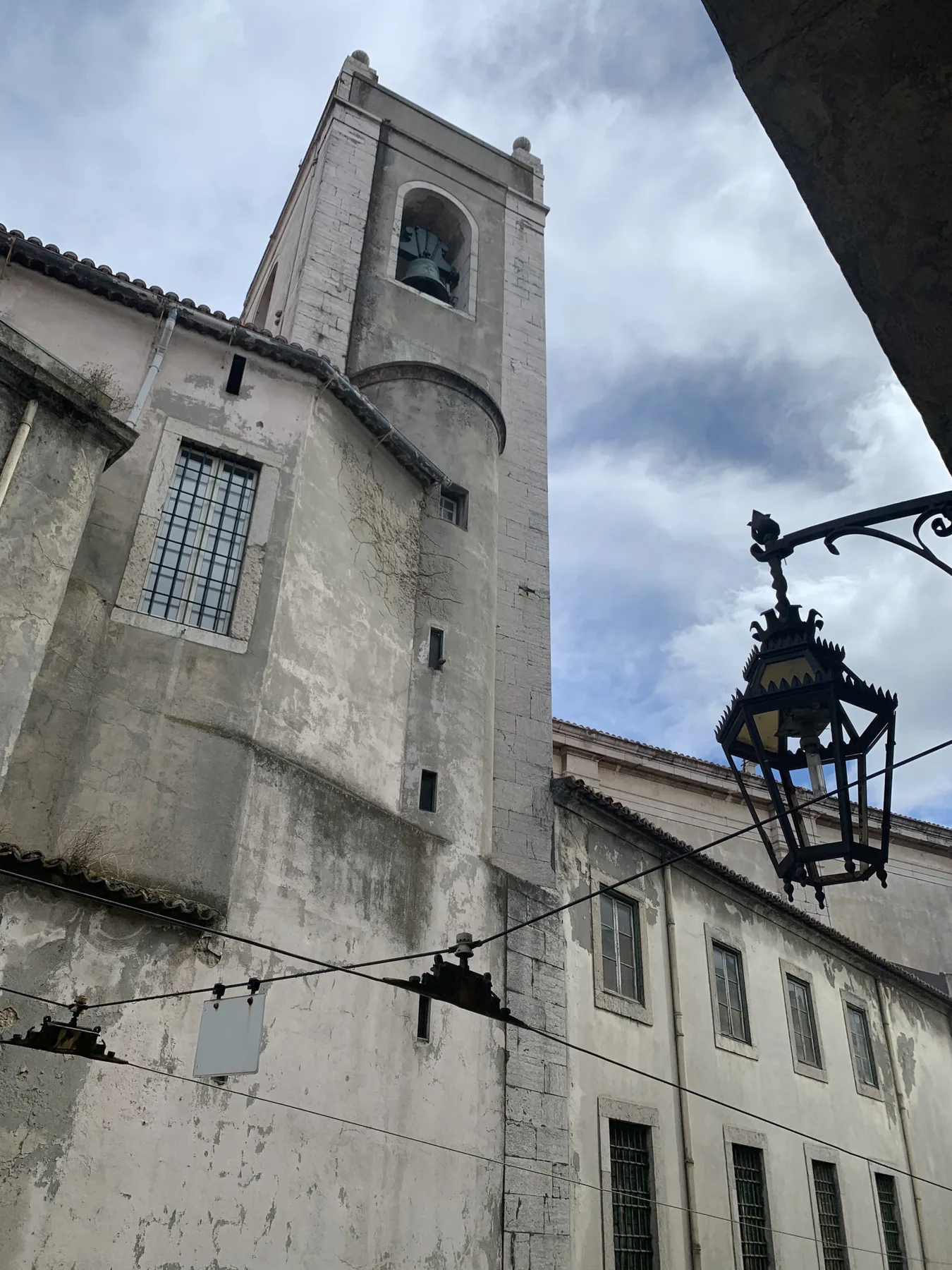 A stone church tower rises above an adjoining building beneath a cloudy sky.