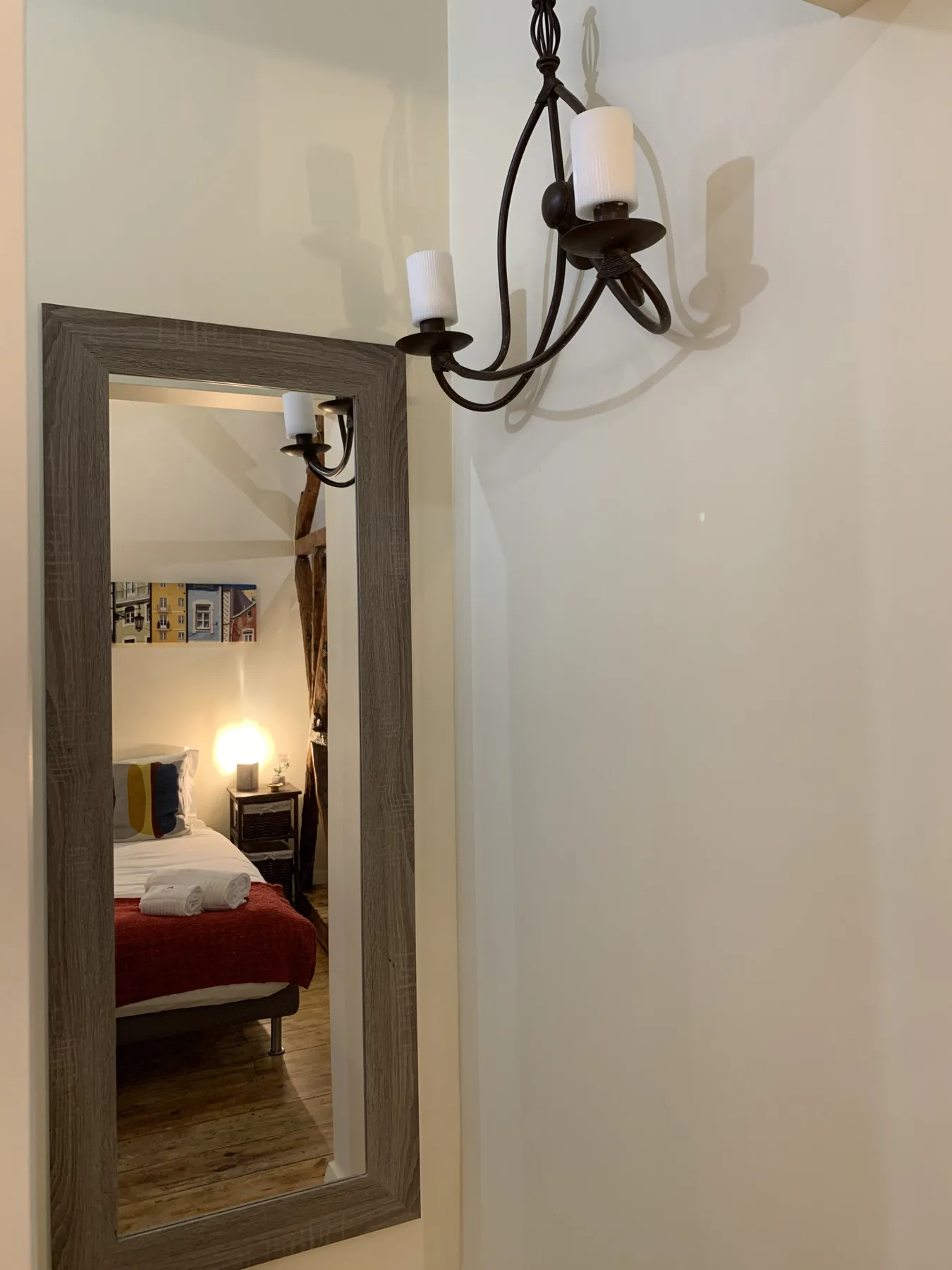 A wall mirror and hanging light overlook a bedroom with a bed and bedside lamp.