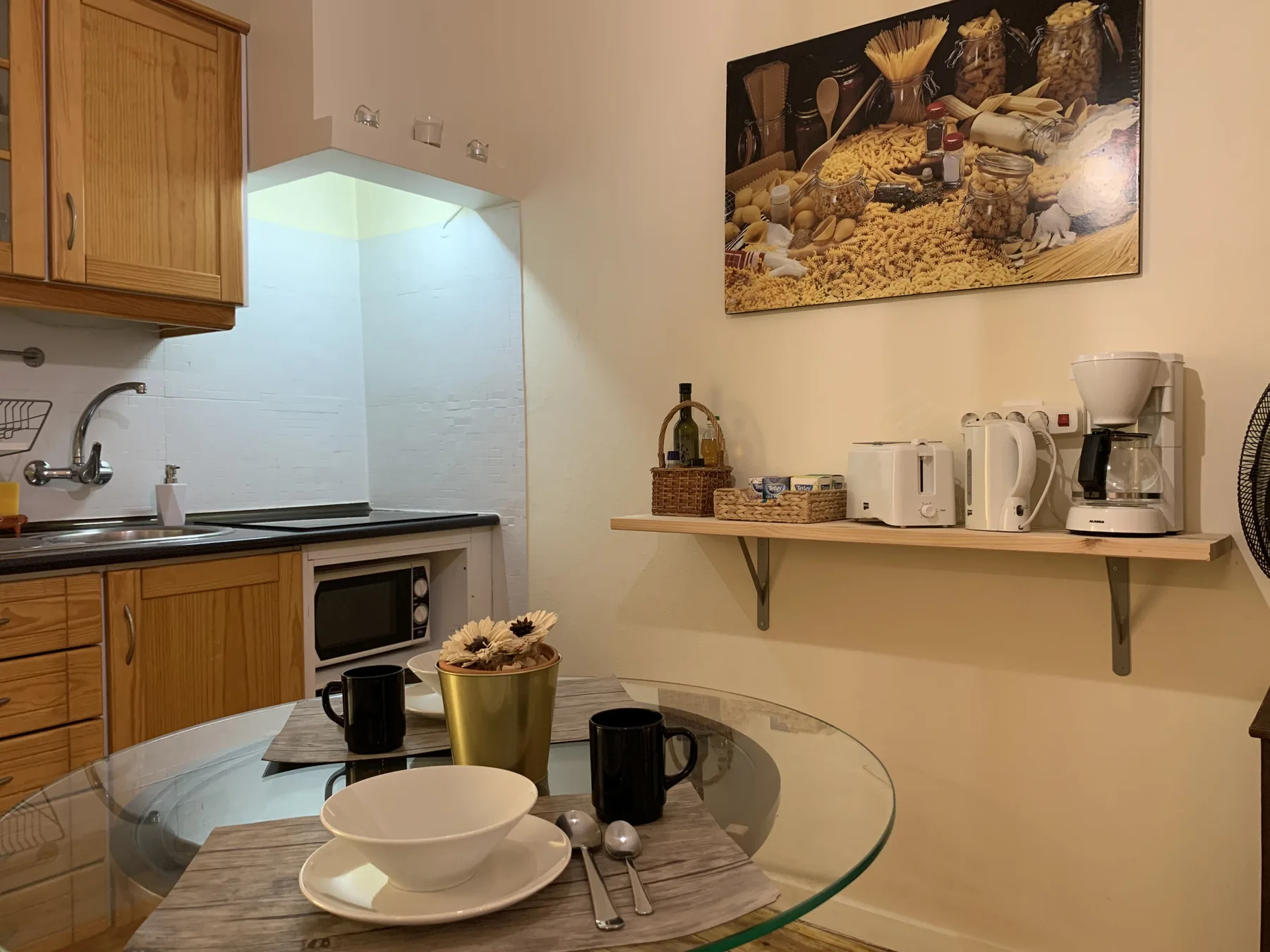 A compact kitchen and dining area with wooden cabinets and a glass table.
