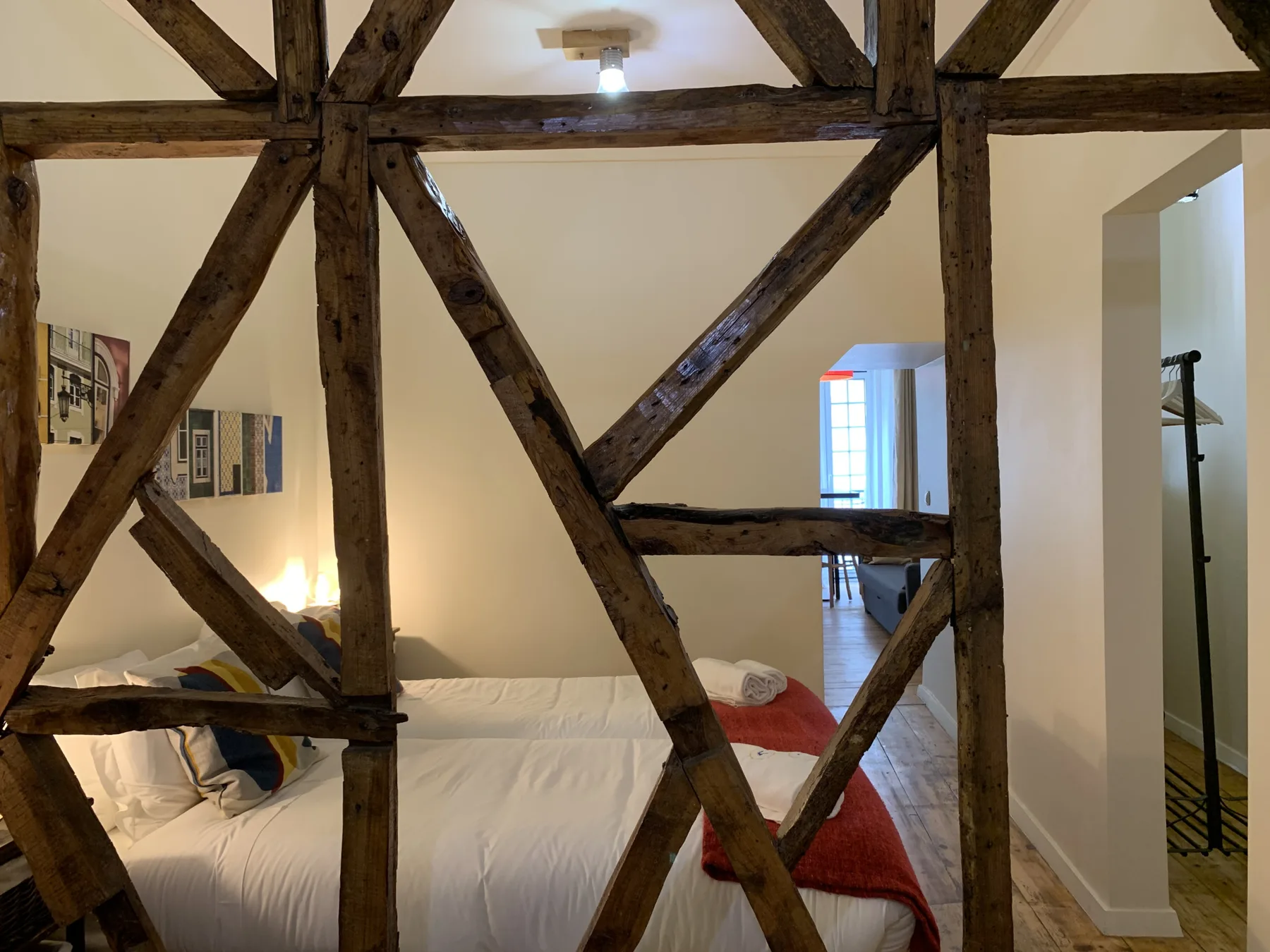 A bedroom with a bed beneath exposed wooden beams and a small window.