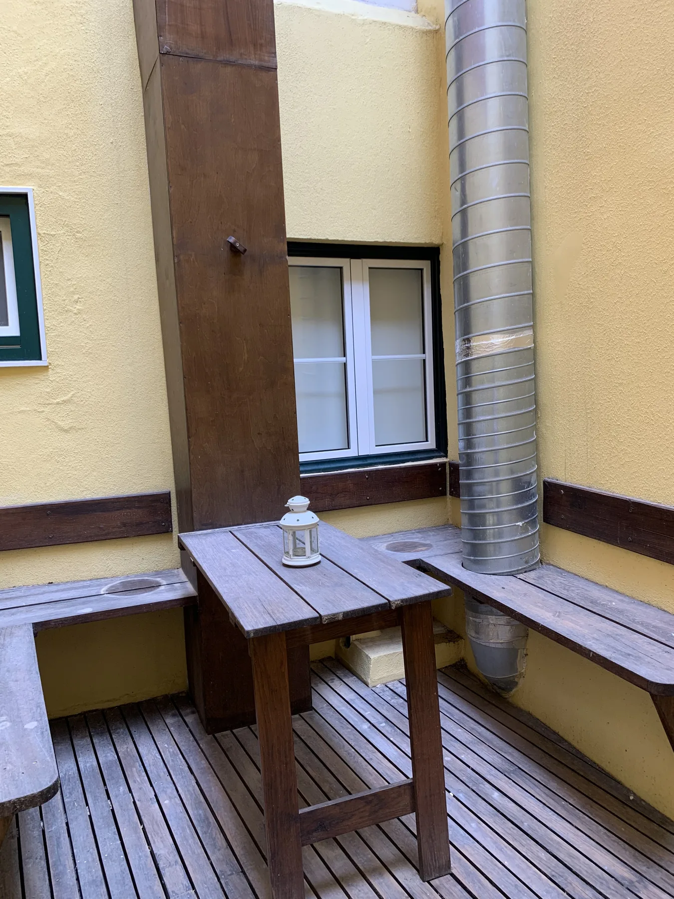 A small patio with wooden seating and a table beside a window.