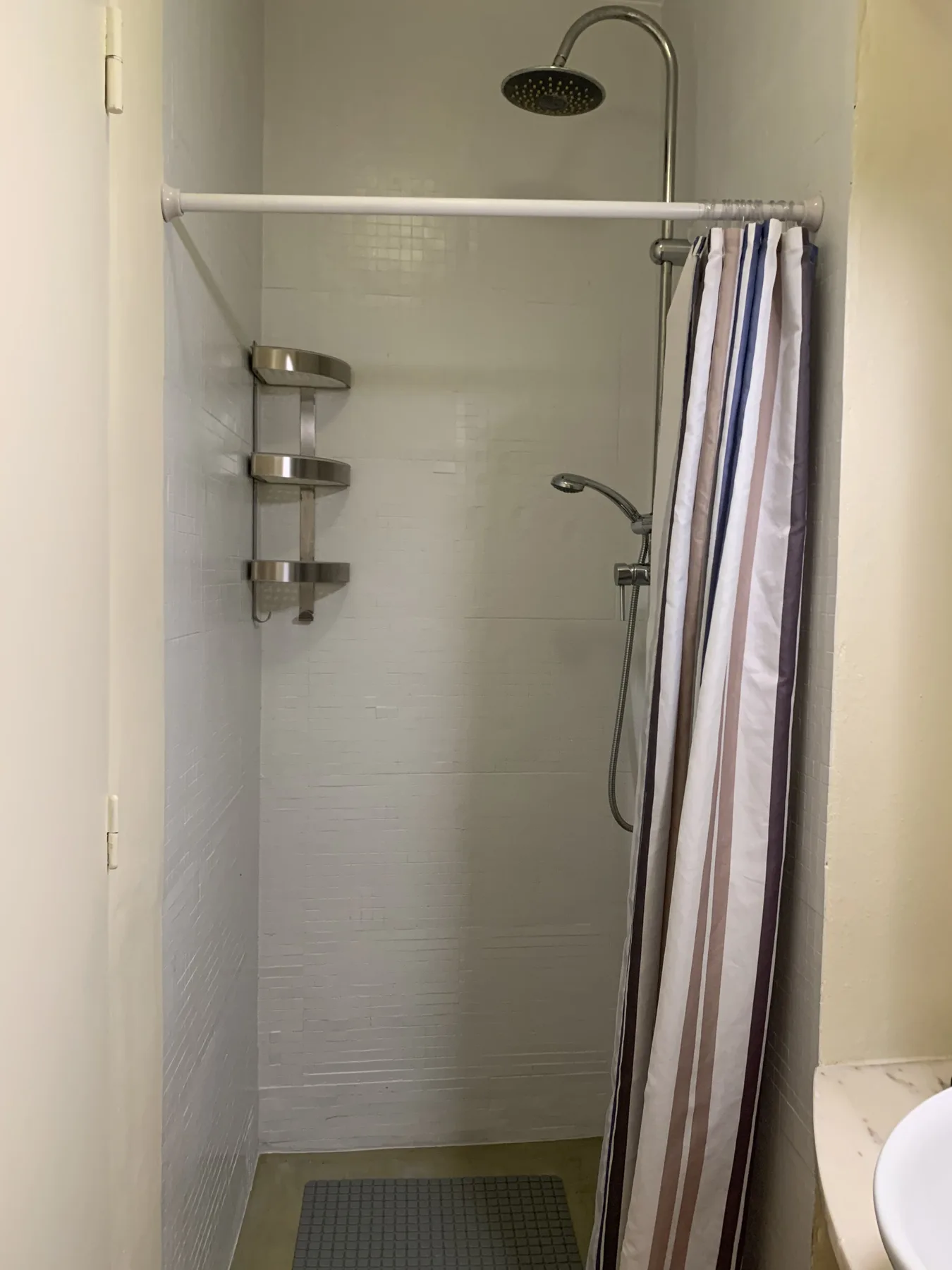 A tiled shower with a striped curtain and wall-mounted shelves.