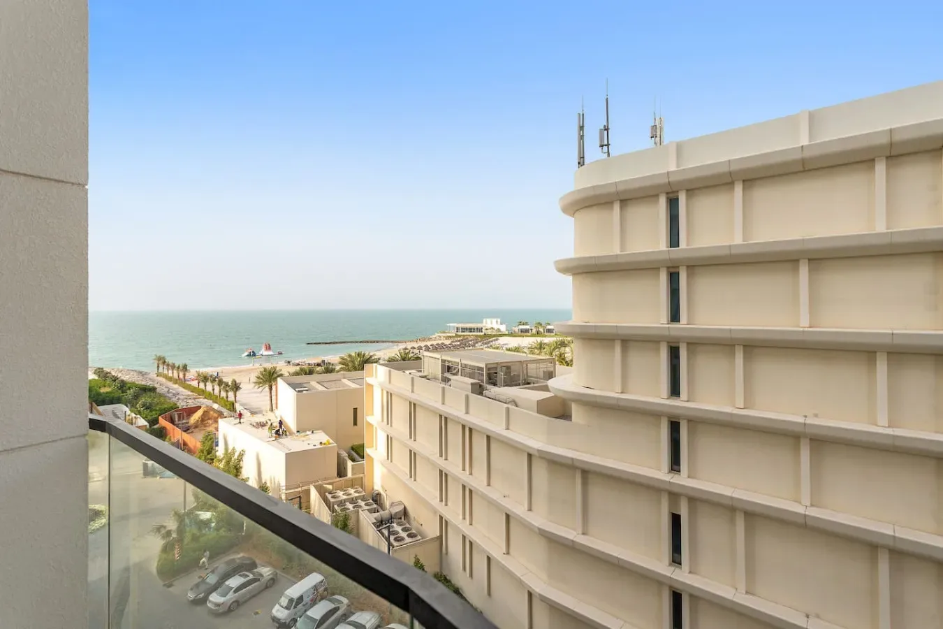 Un balcón da a edificios cercanos, una playa y el mar.