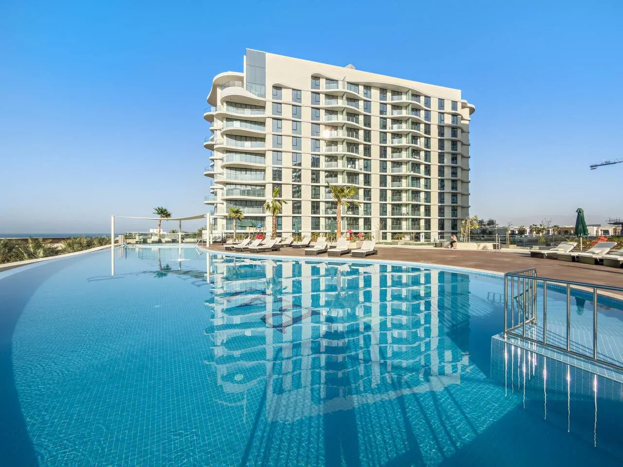 Una gran piscina al aire libre refleja un edificio de varios pisos bajo un cielo despejado.