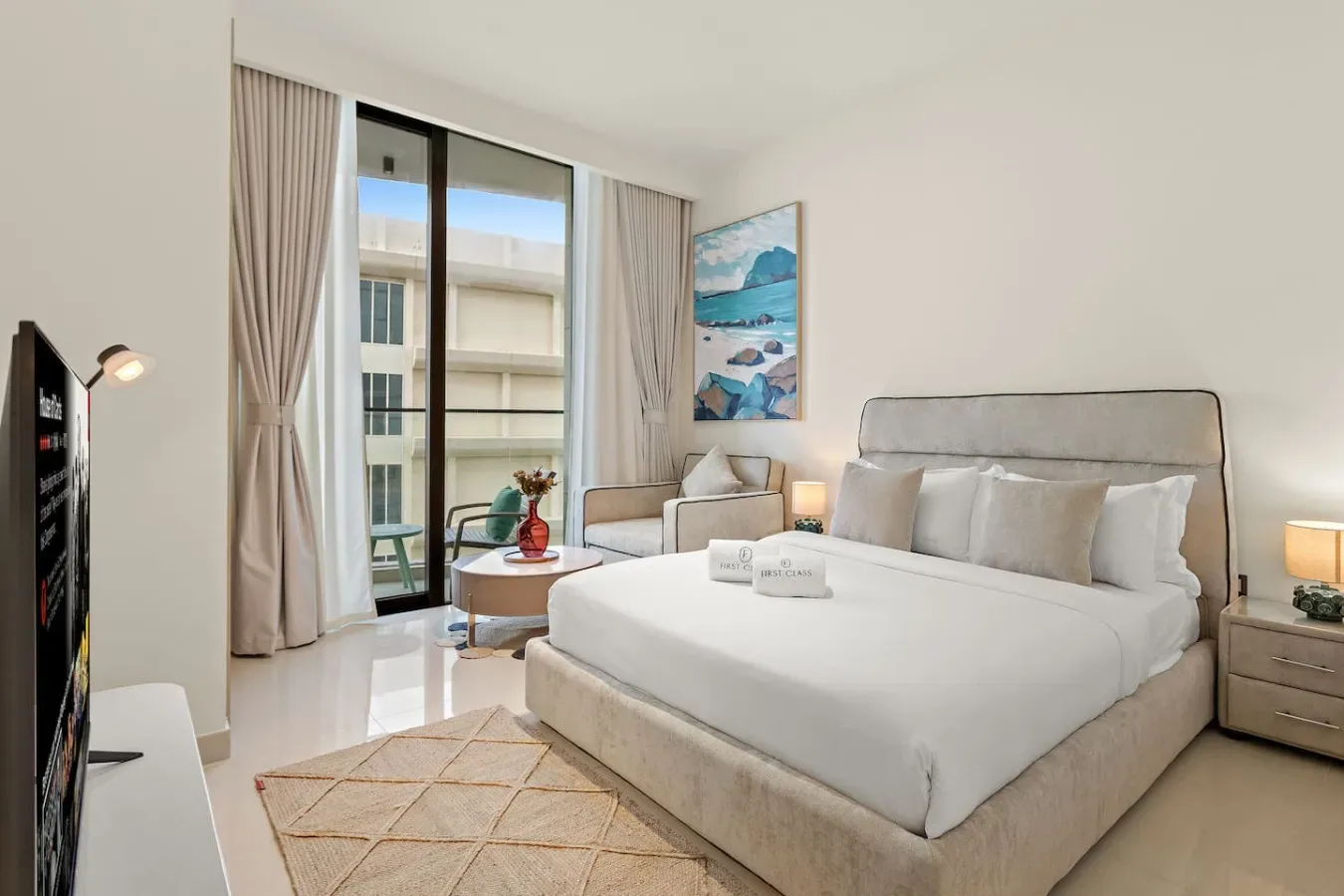 Un dormitorio luminoso con una cama grande, una zona de estar y ventanas altas con cortinas.