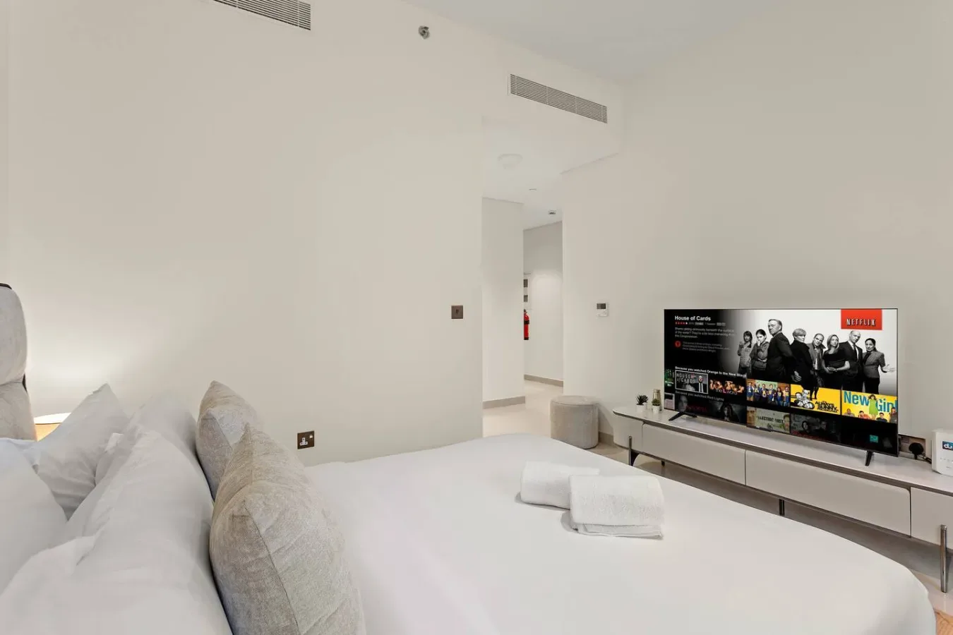 Un dormitorio luminoso con una cama, toallas dobladas y un televisor sobre un mueble bajo.