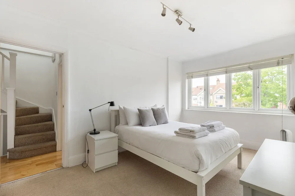 Un dormitorio luminoso con cama, mesita de noche y grandes ventanas.