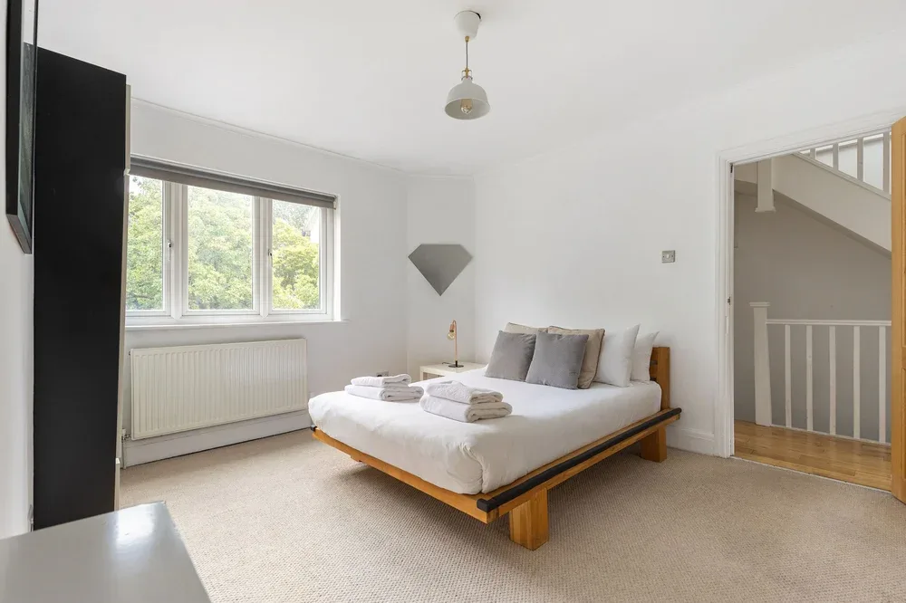 A bright bedroom with a double bed beside a window.